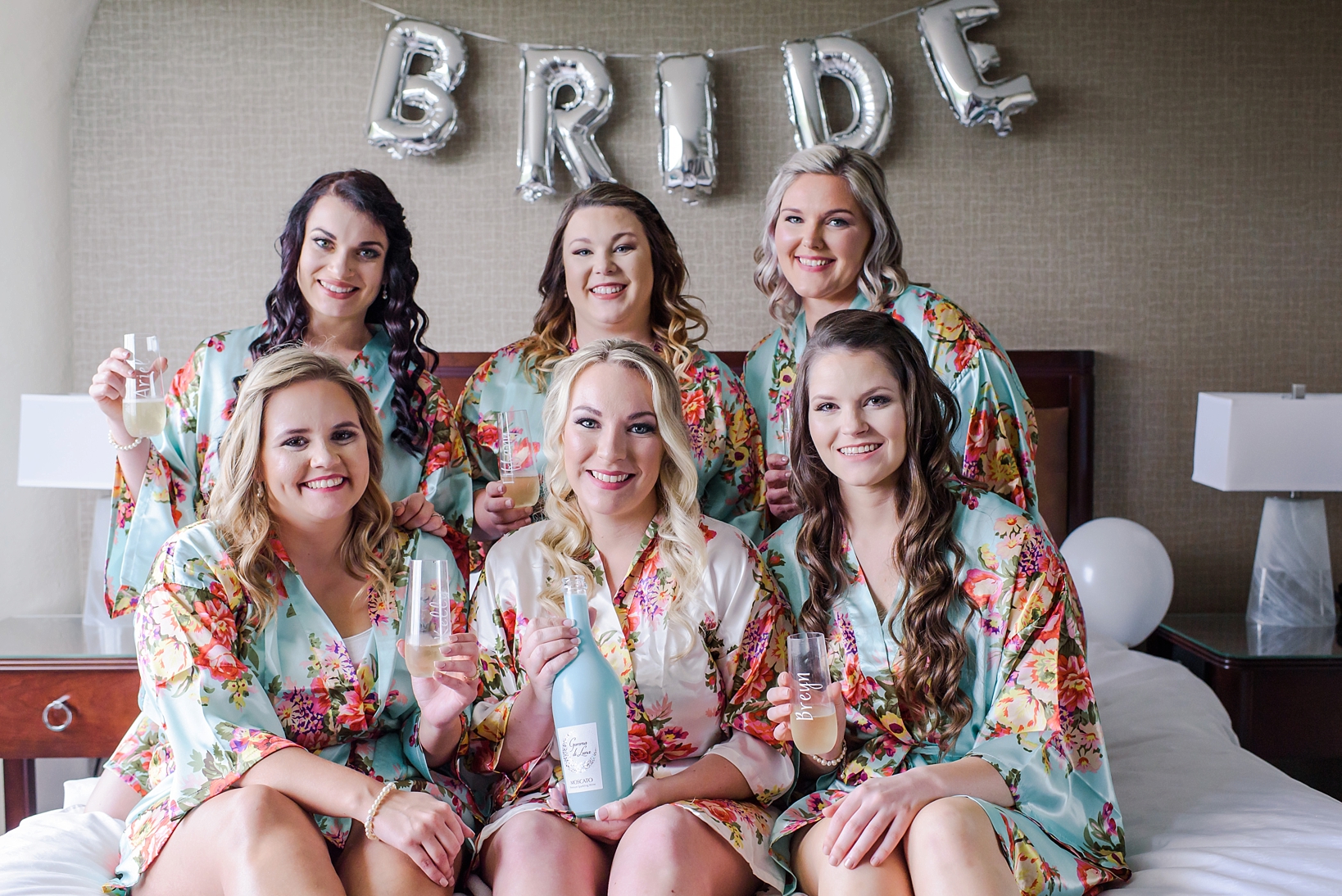 Bride and her bridesmaids in floral robes holding champagne bottle and glasses