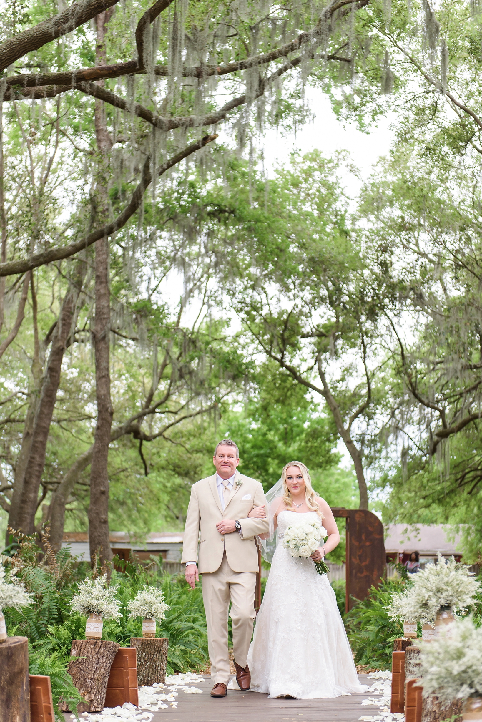 Bride and her father walking down the aisle surrounded by greenery