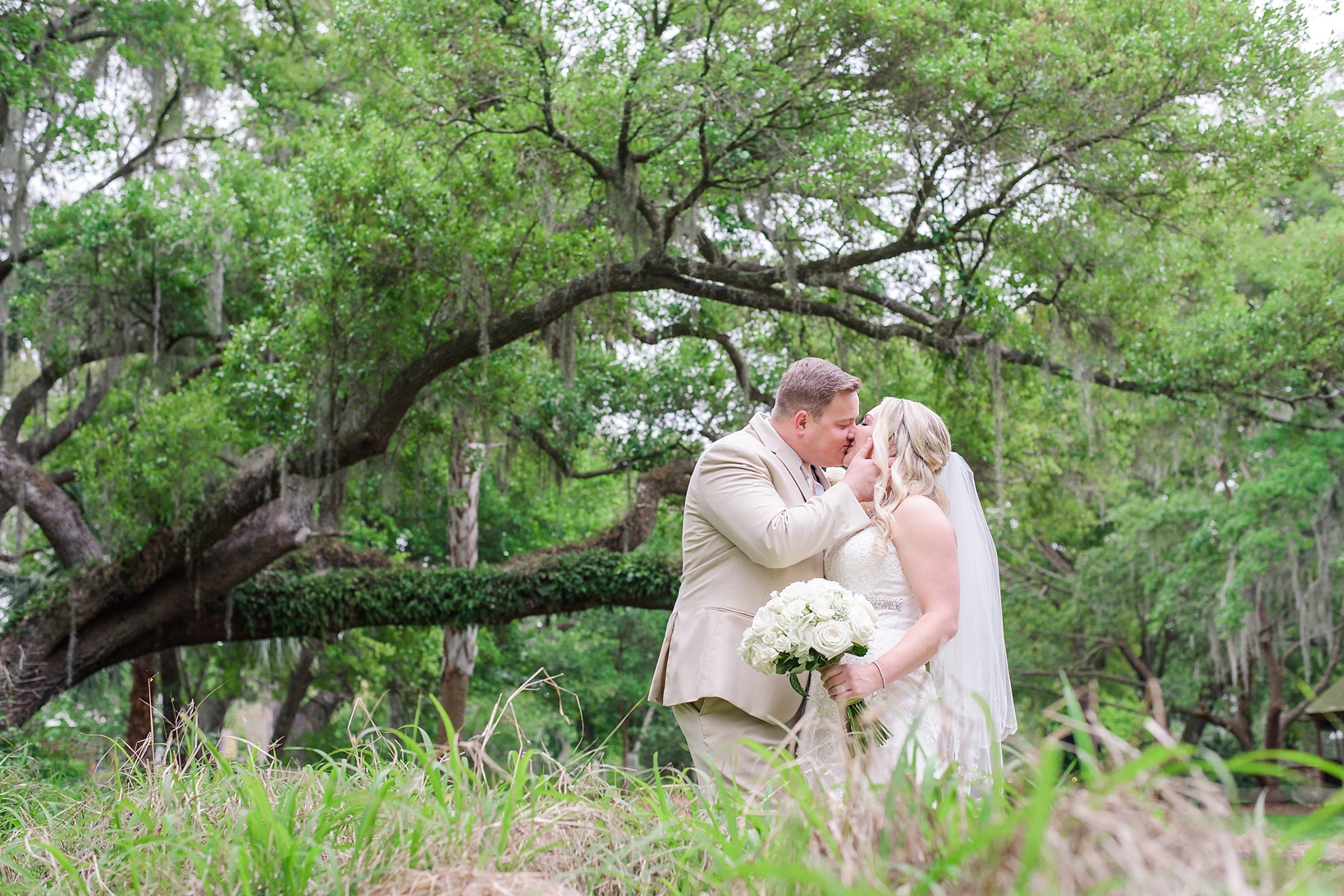 Florida rustic wedding bridal photo of Groom kissing his bride under the ancient oaks of cross creek ranch 