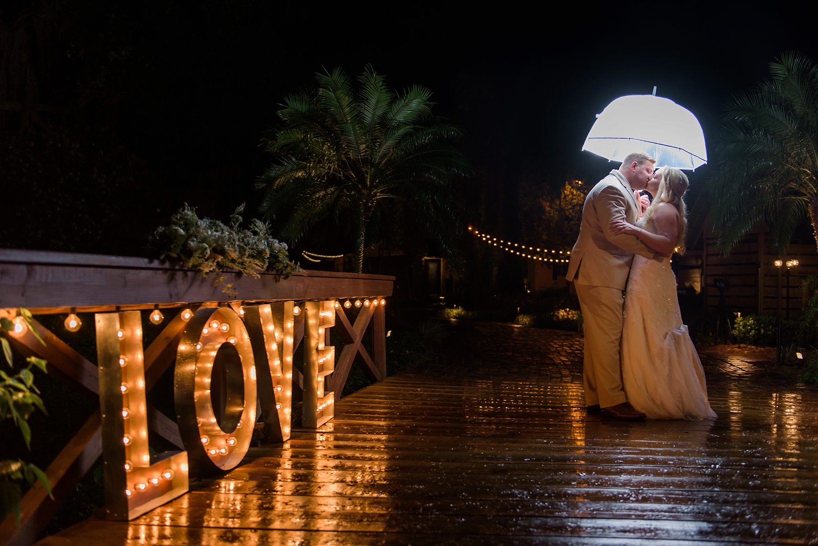 Bride and Groom with umbrella and Love sign lit up on a rainy bridge after their cross creek ranch reception