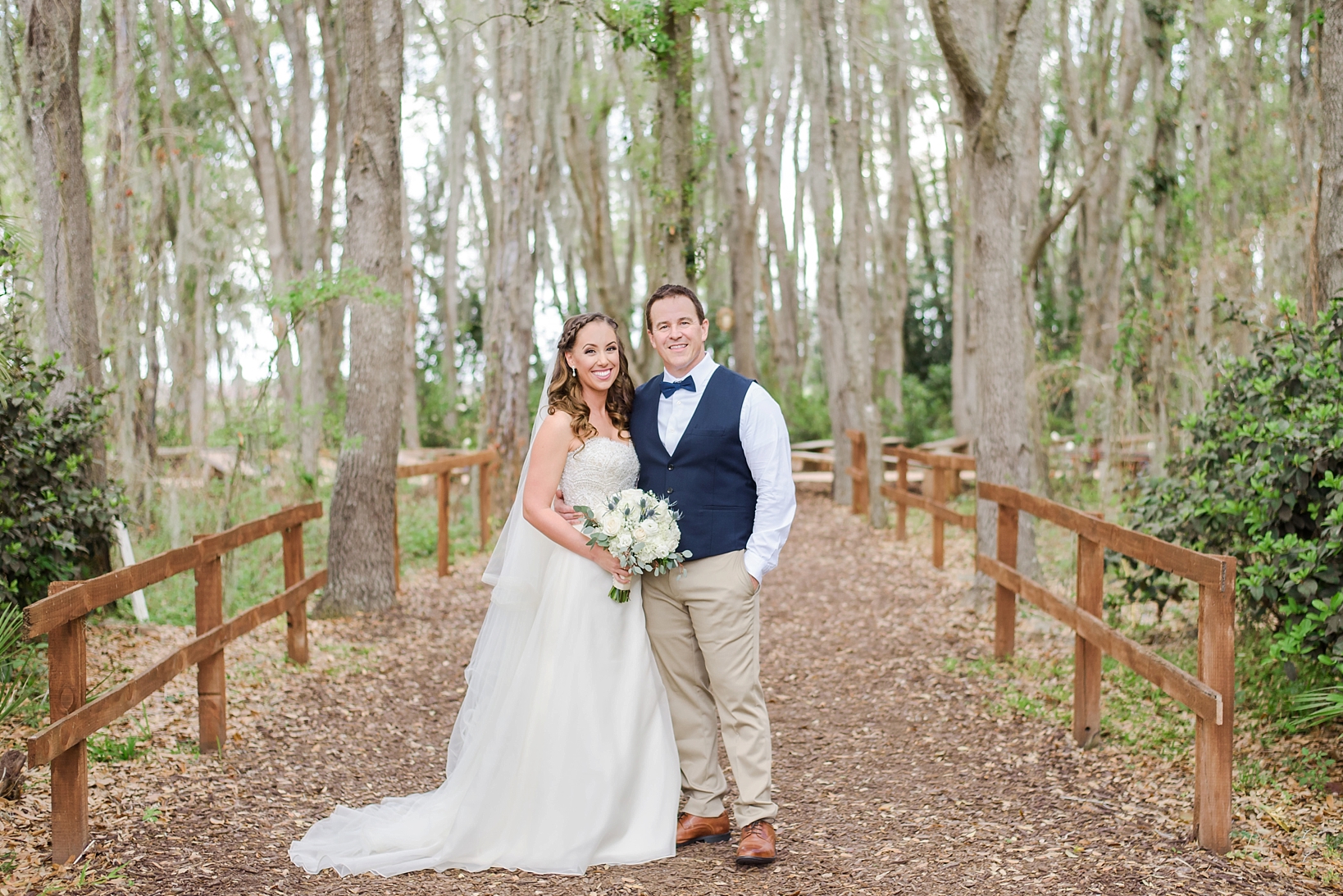 Bride and Groom pose under a tunnel of large trees and a pathway