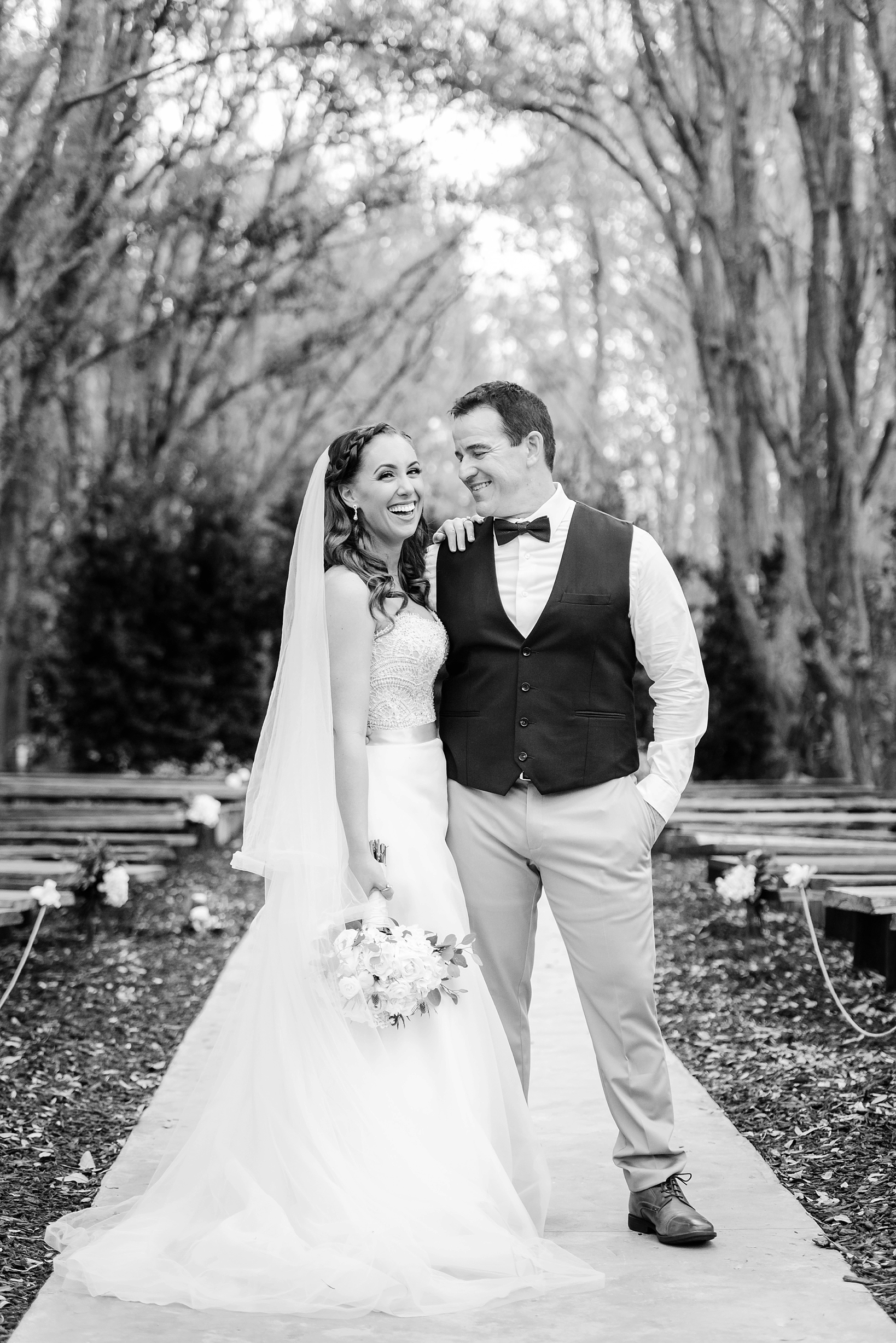 Bride laughing at her groom as he smiles back at her under an arch of oak trees in Florida by Sarah & Ben Photography