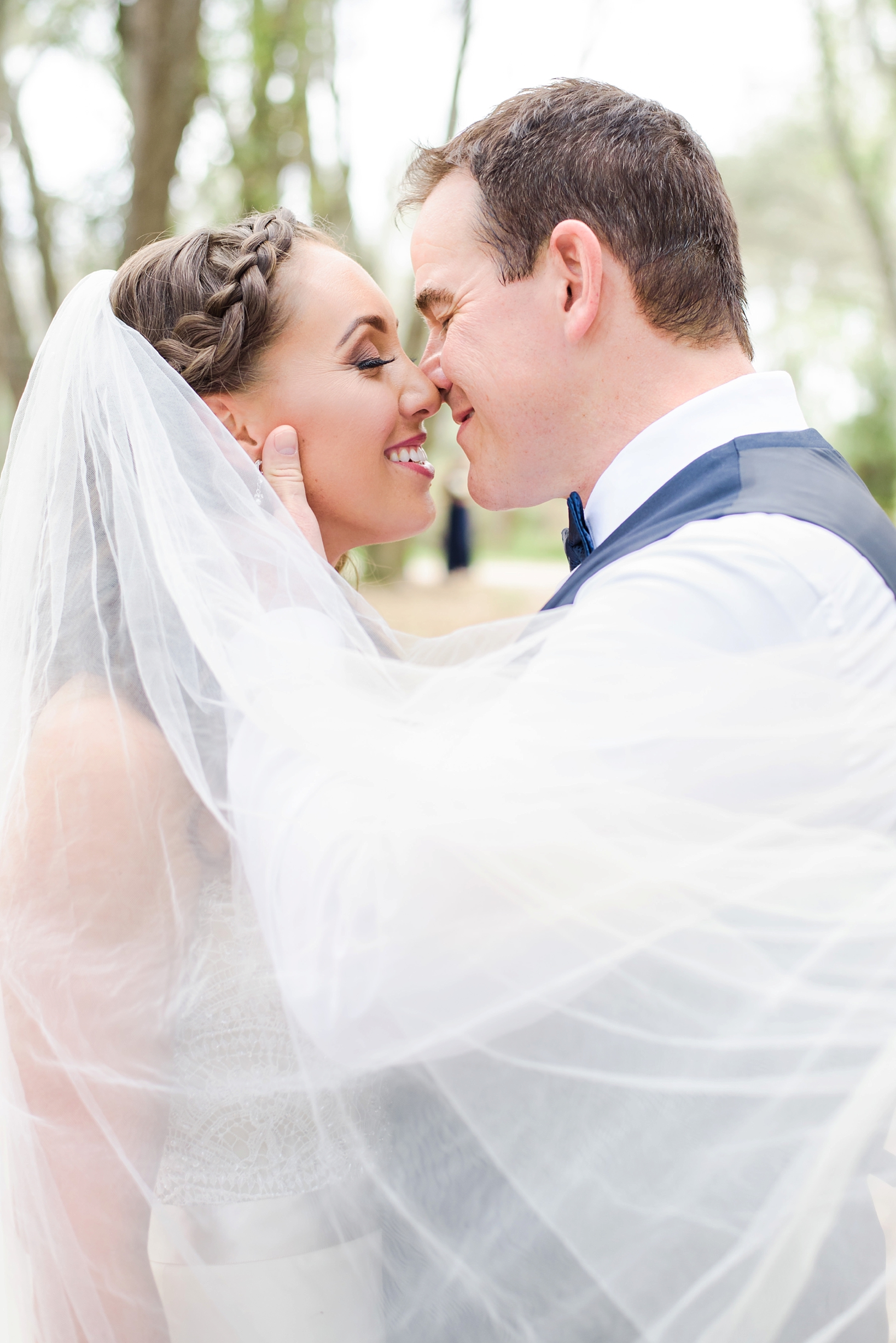 Bride and Groom smiling while they kiss as the wind blows the veil around them