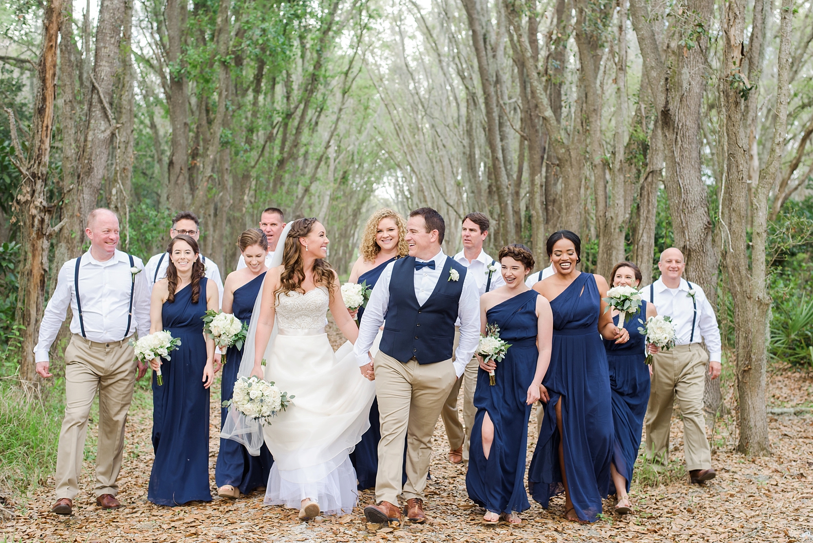 The wedding Bridal Party walking through the woods towards the ceremony by Sarah & Ben Photography