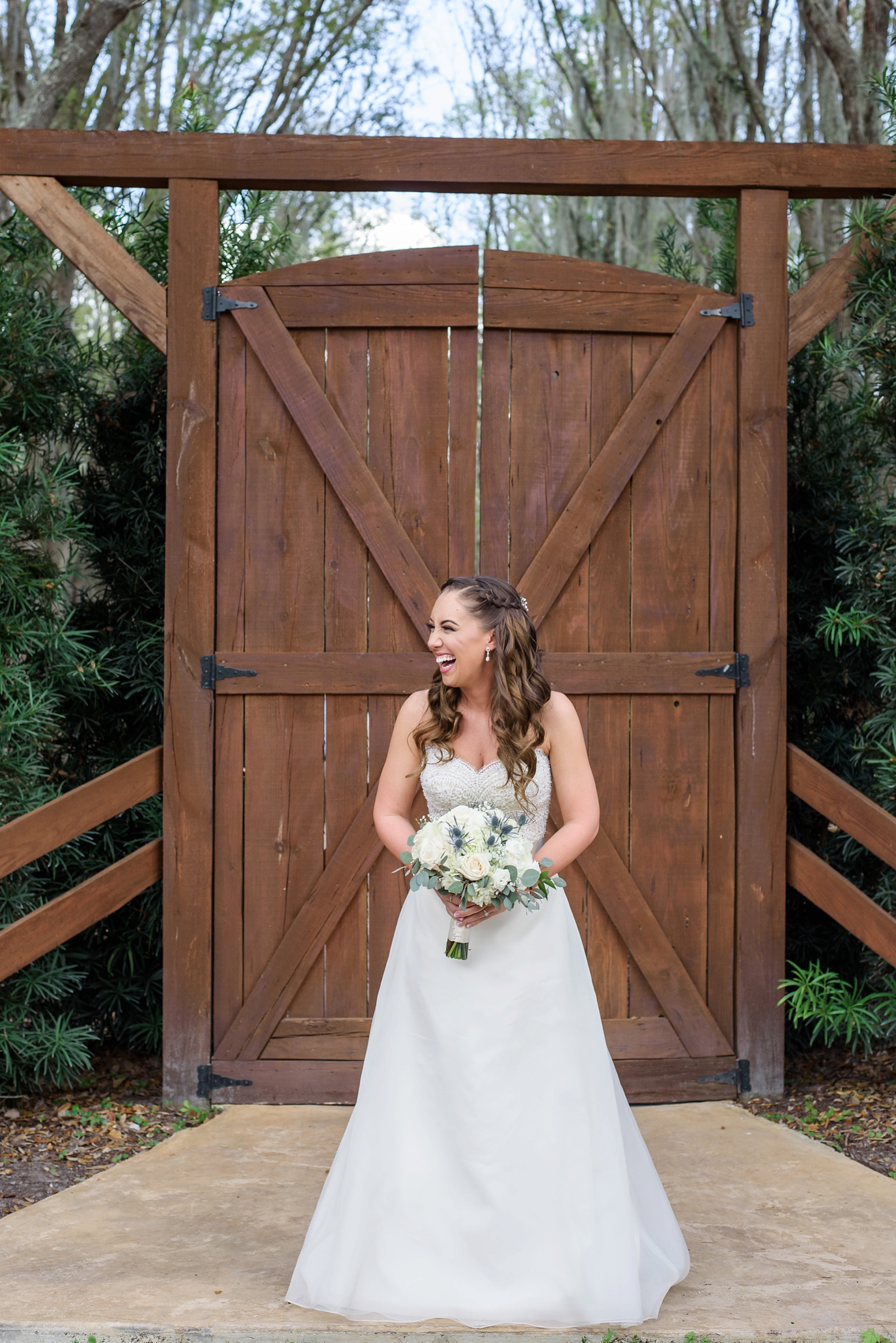 Bride laughing during portraits in front of a large rustic door leading to the ceremony by Sarah & Ben Photography