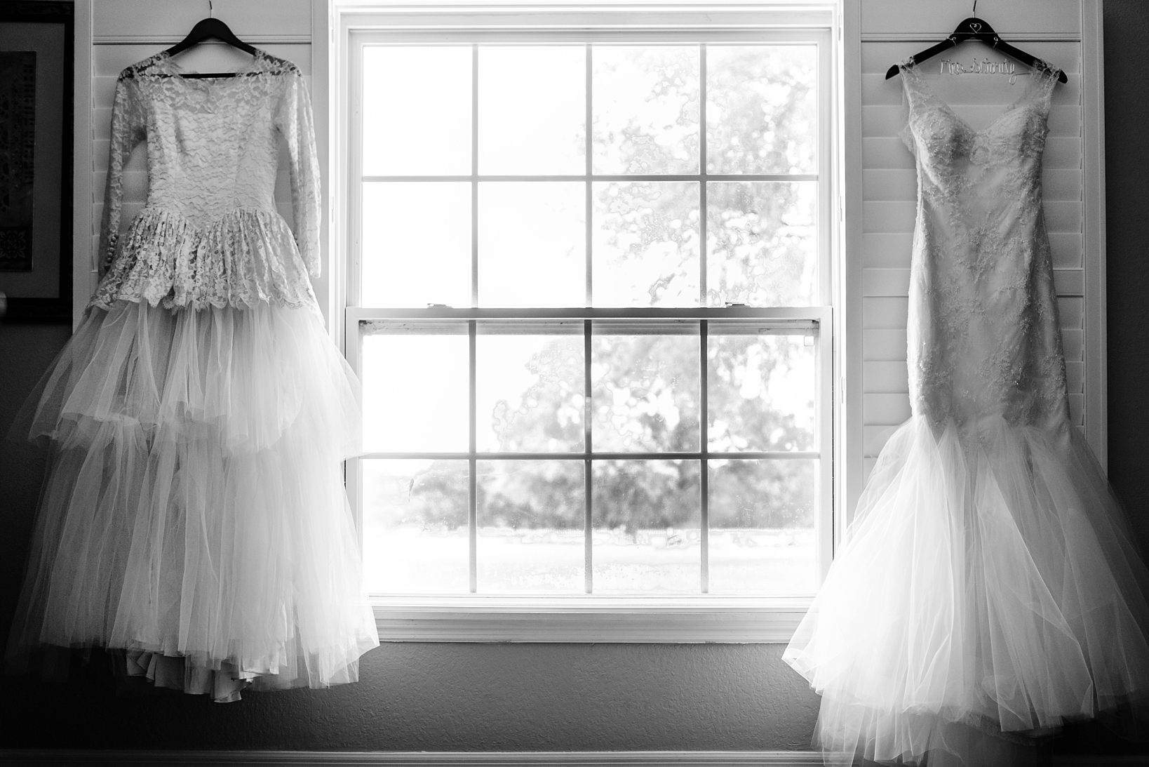 Bride's wedding dress and her grandmother's wedding dress hanging together in the window