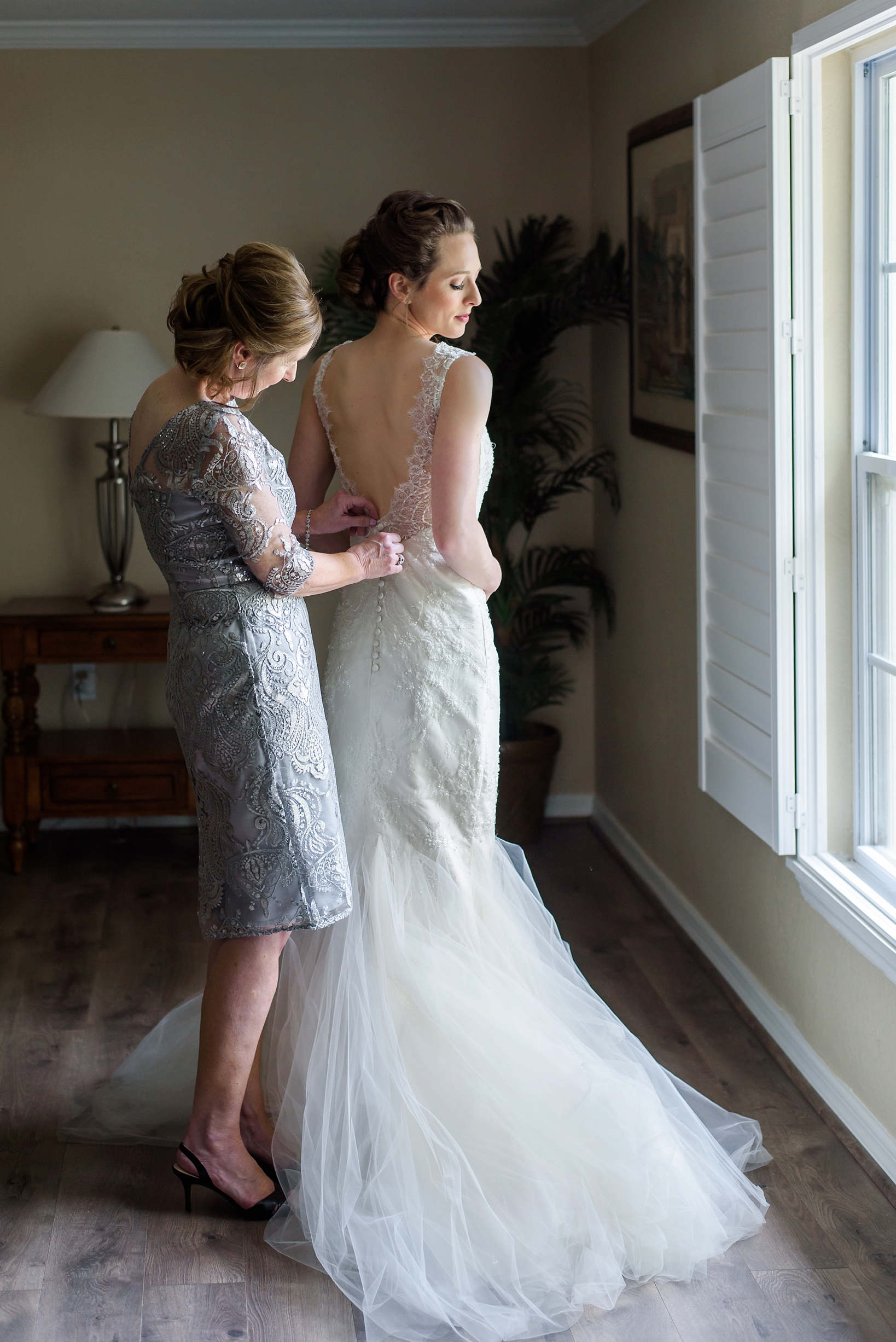 Mother of the bride helping her daughter into her wedding dress by Sarah & Ben Photography