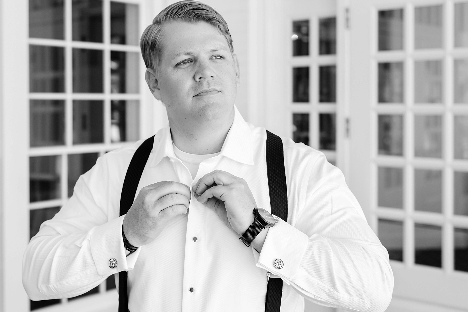 Groom putting his shirt buttons in while wearing suspenders