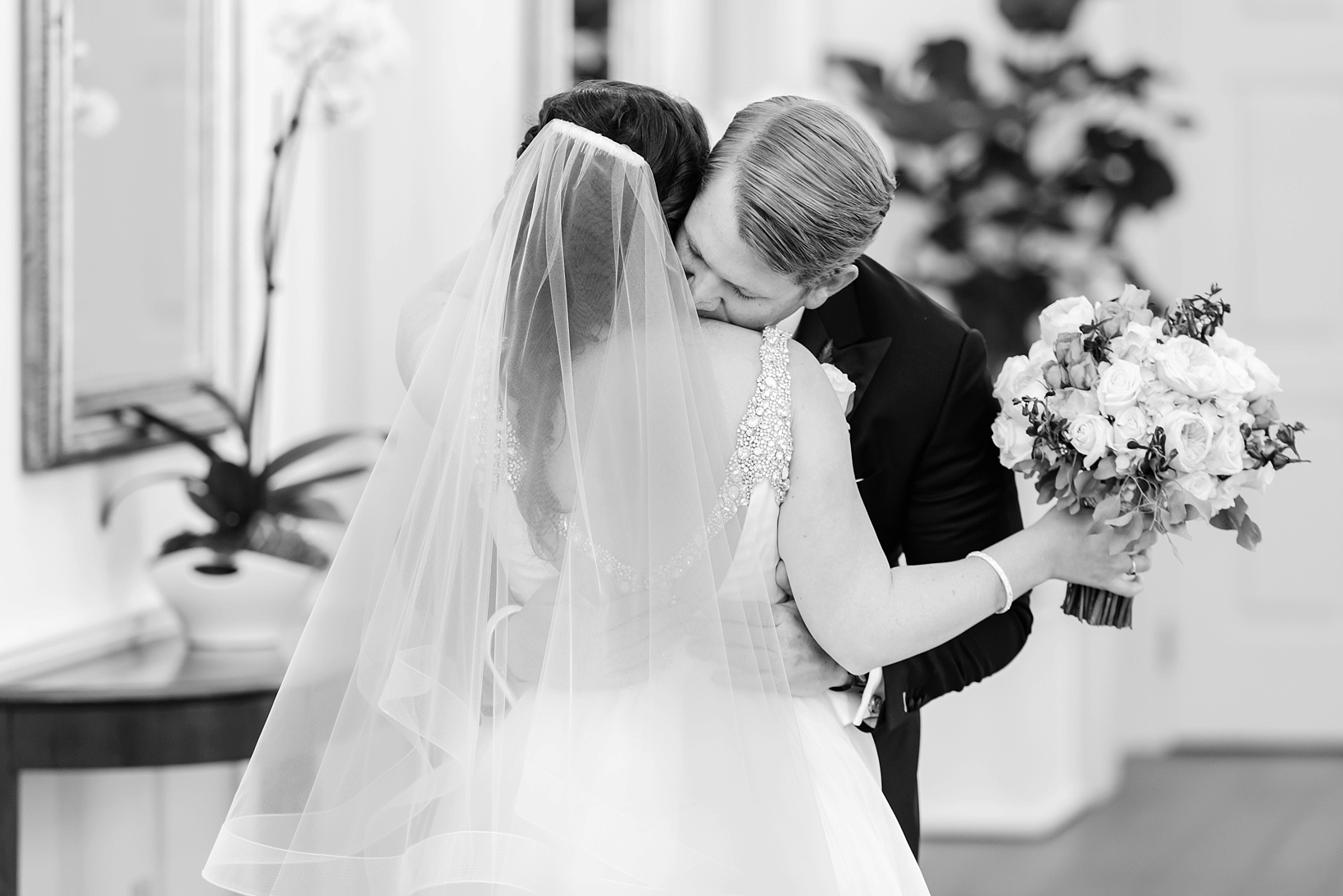 Groom kisses the neck of his bride as she holds her floral bouquet