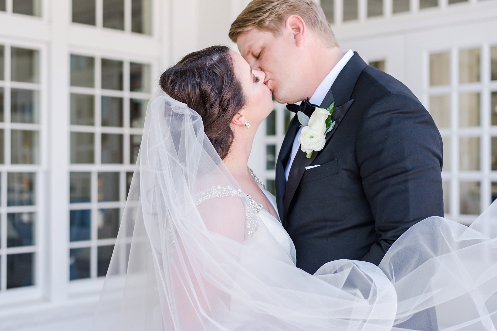 Bride and groom kissing as the wind blows the veil by Sarah & Ben Photography