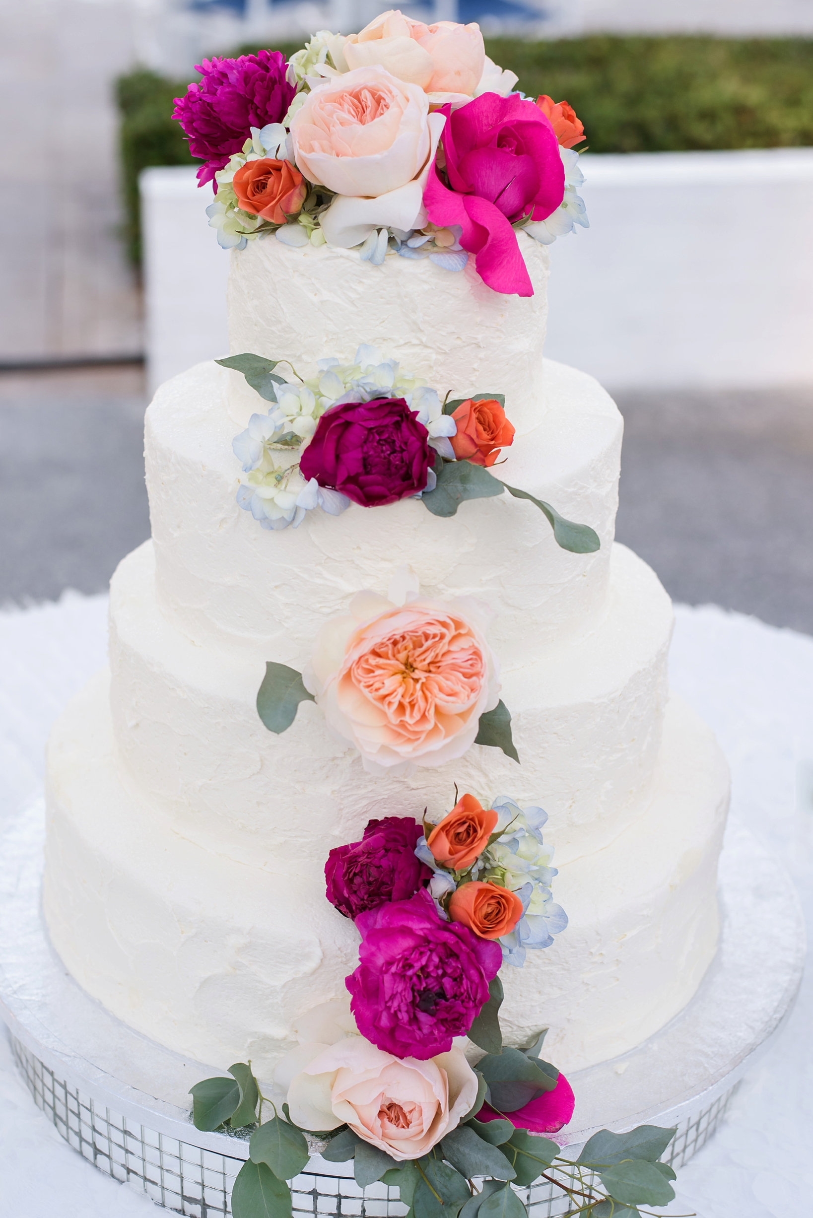 The wedding cake with huge colorful flowers and eucalyptus leaves by Sarah & Ben Photography