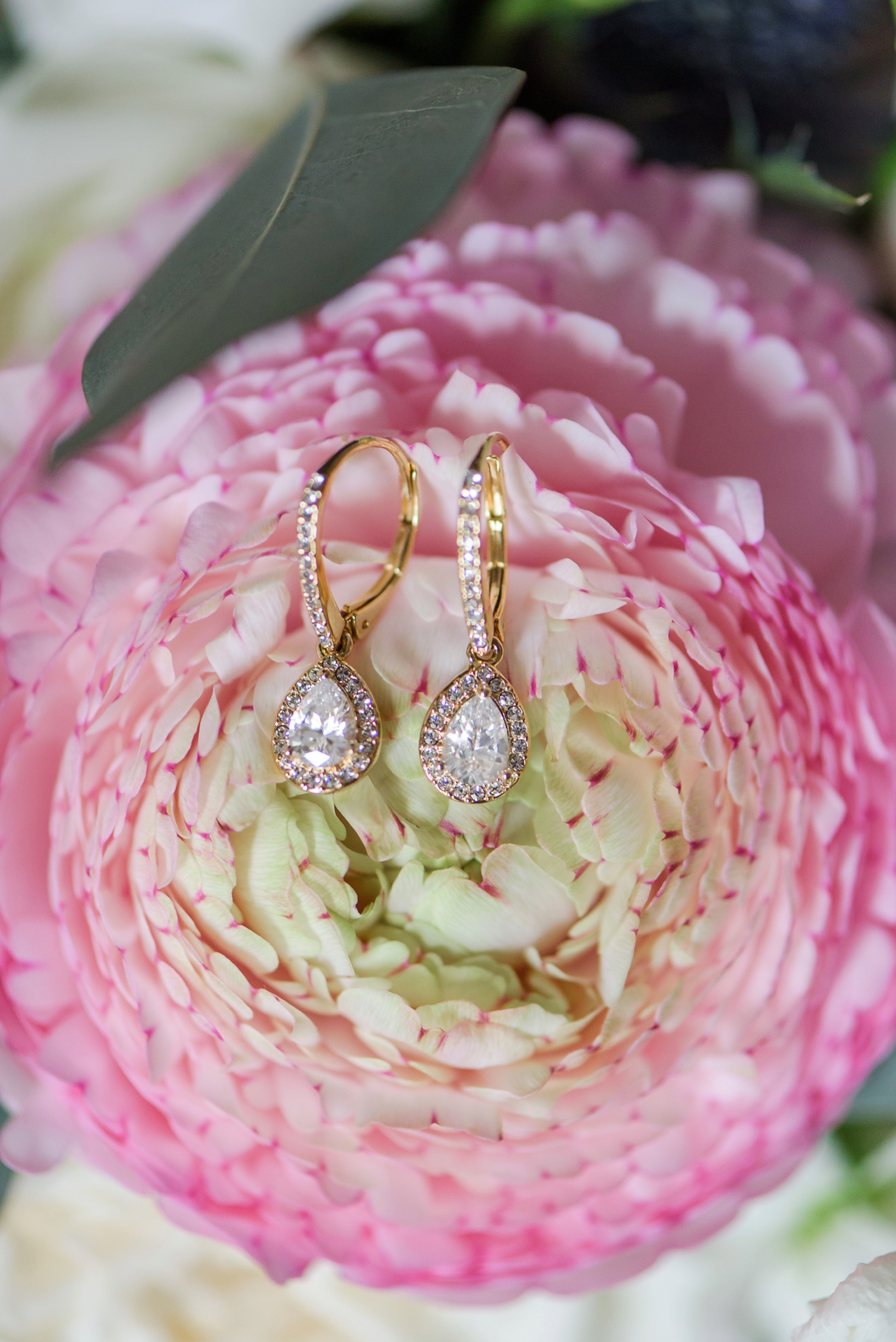 Gold bridal earrings against the floral background of the bouquet