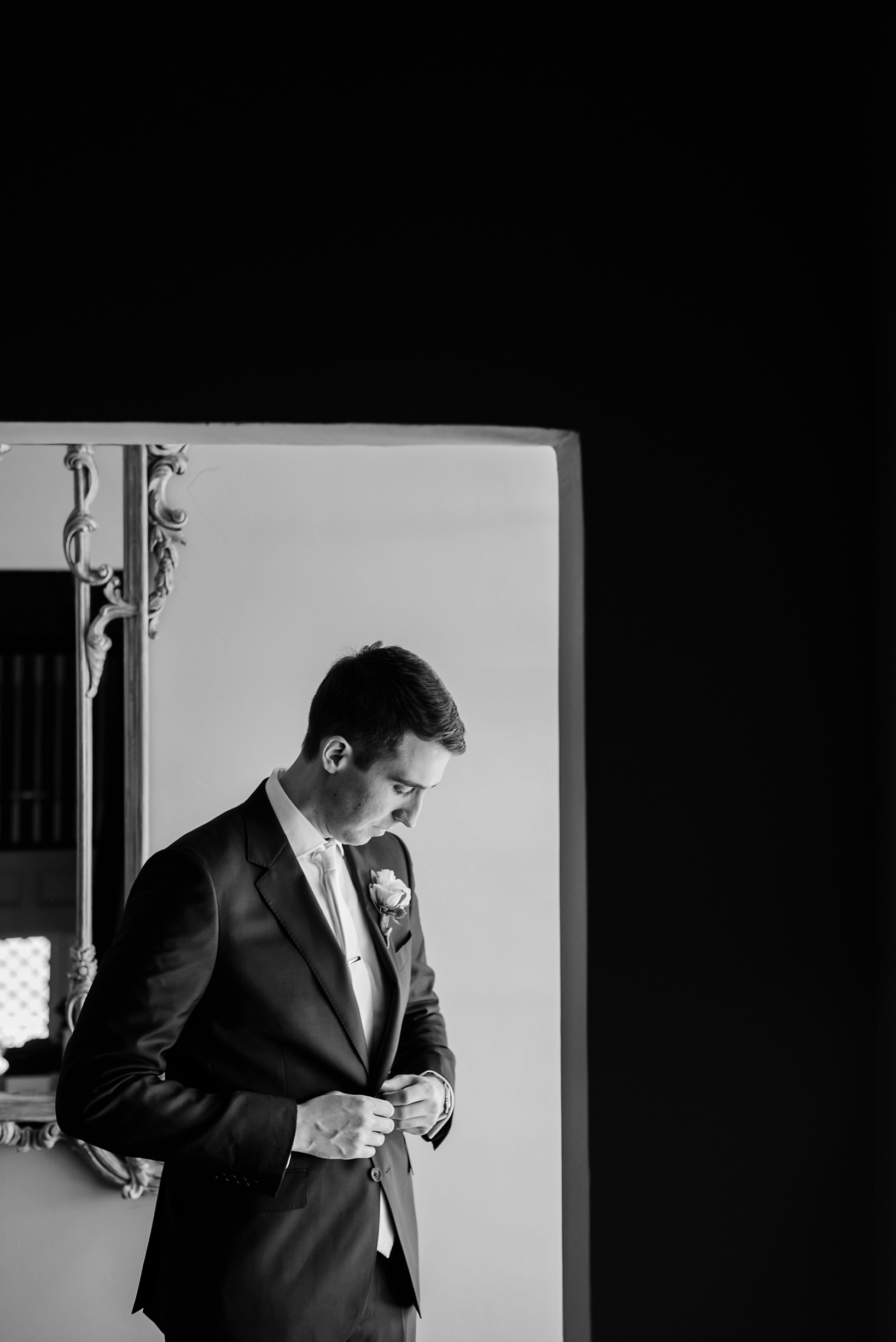 The groom in an asymmetrical framing pose adjusting his suit jacket