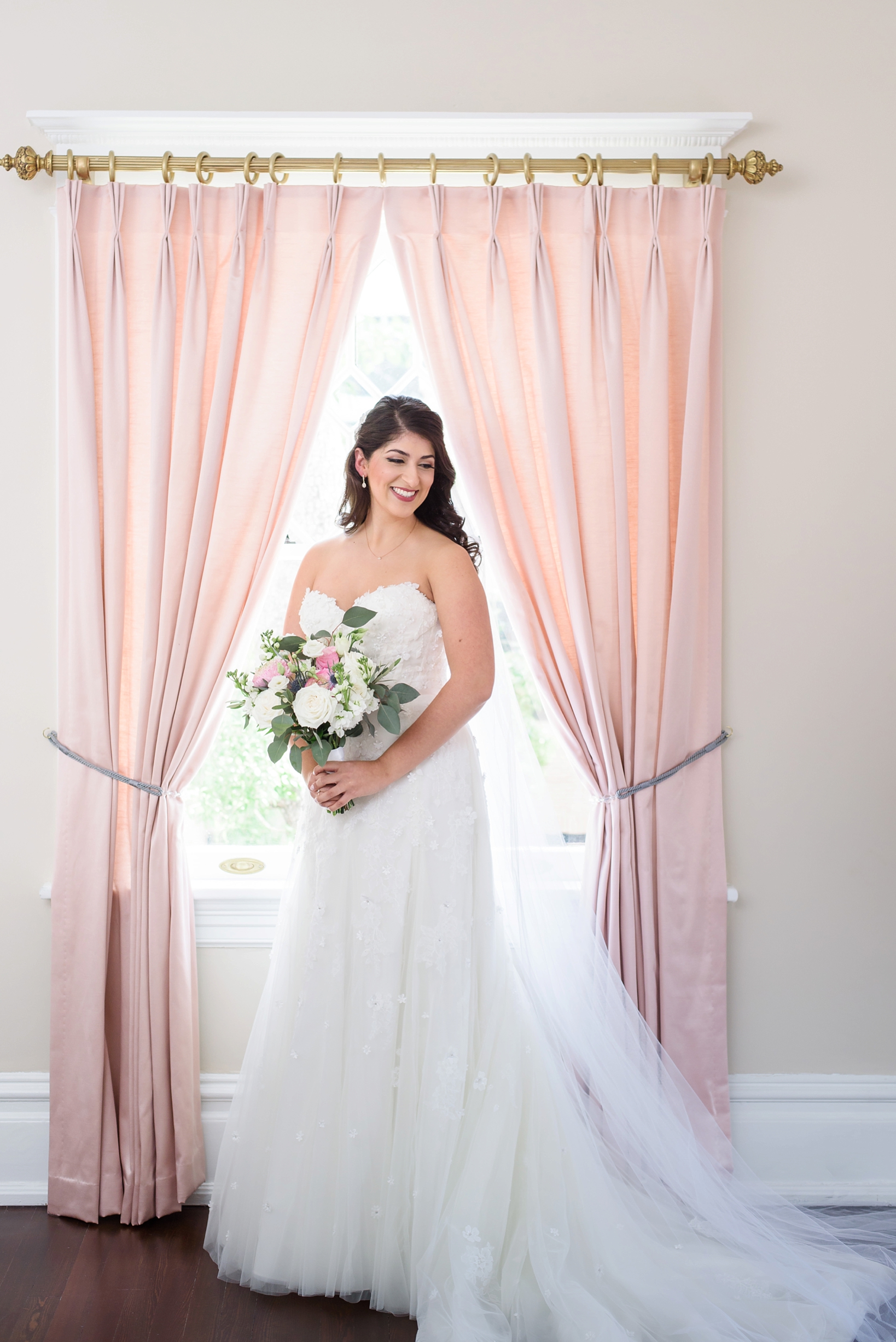 The bride holding her flowers in the arch of a window