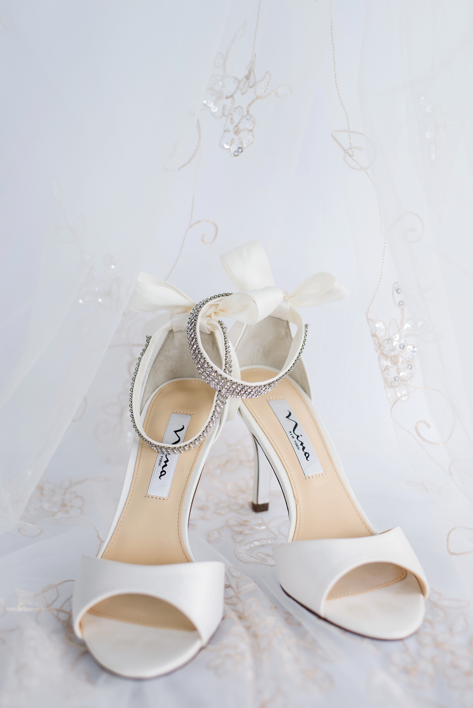Bride's rhinestone and bow heels surrounded by her wedding veil by Sarah & Ben Photography