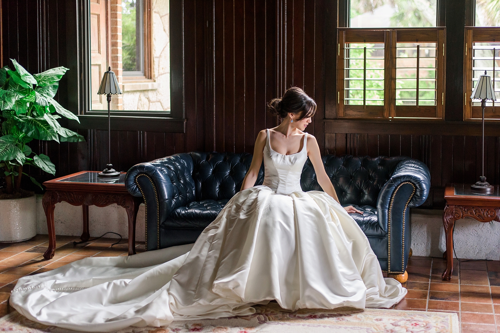 Timeless image of a bride in her dress sitting on a leather tufted sofa by Sarah & Ben Photography