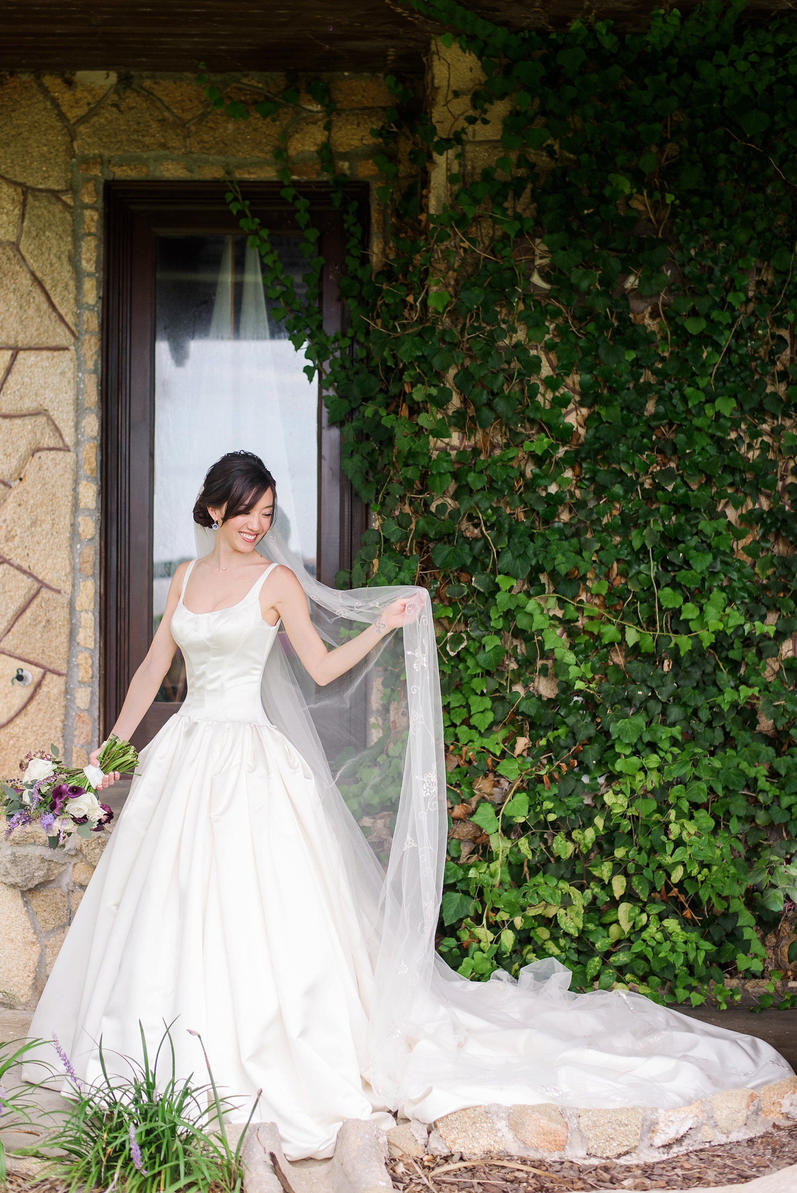 The bride holding her cathedral veil in one hand and her bouquet in the other by Sarah & Ben Photography
