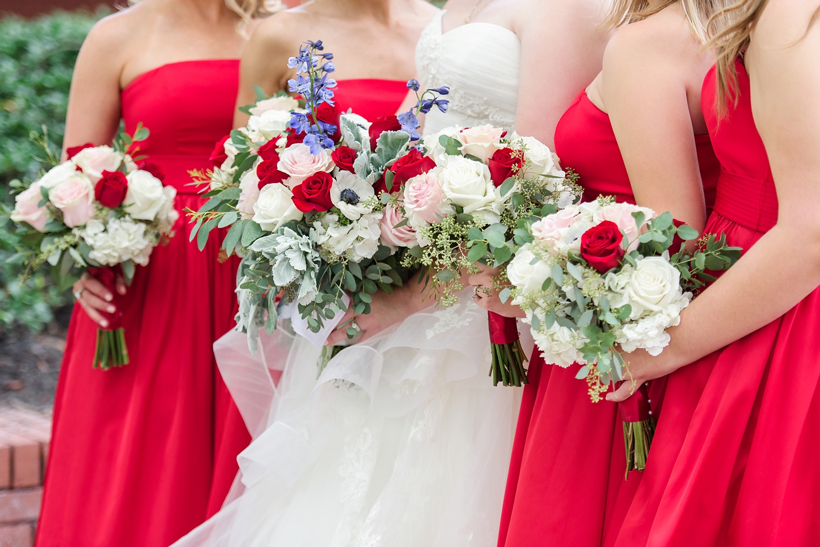 Floral details of the bride and her bridesmaids bouquets popping against the red dresses