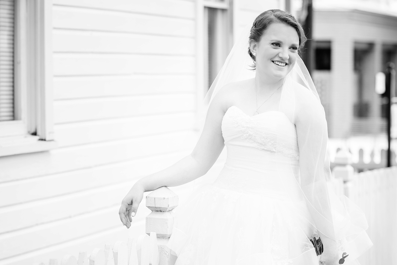 Bride leaning against a white fence in her wedding dress