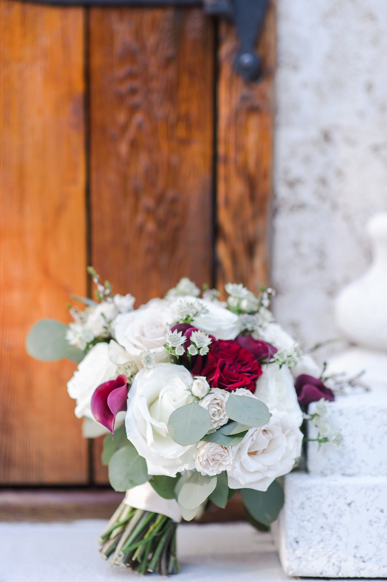 The brides bouquet filled with roses leaning against a stone pillar by Sarah & Ben Photography located in Tampa, FL