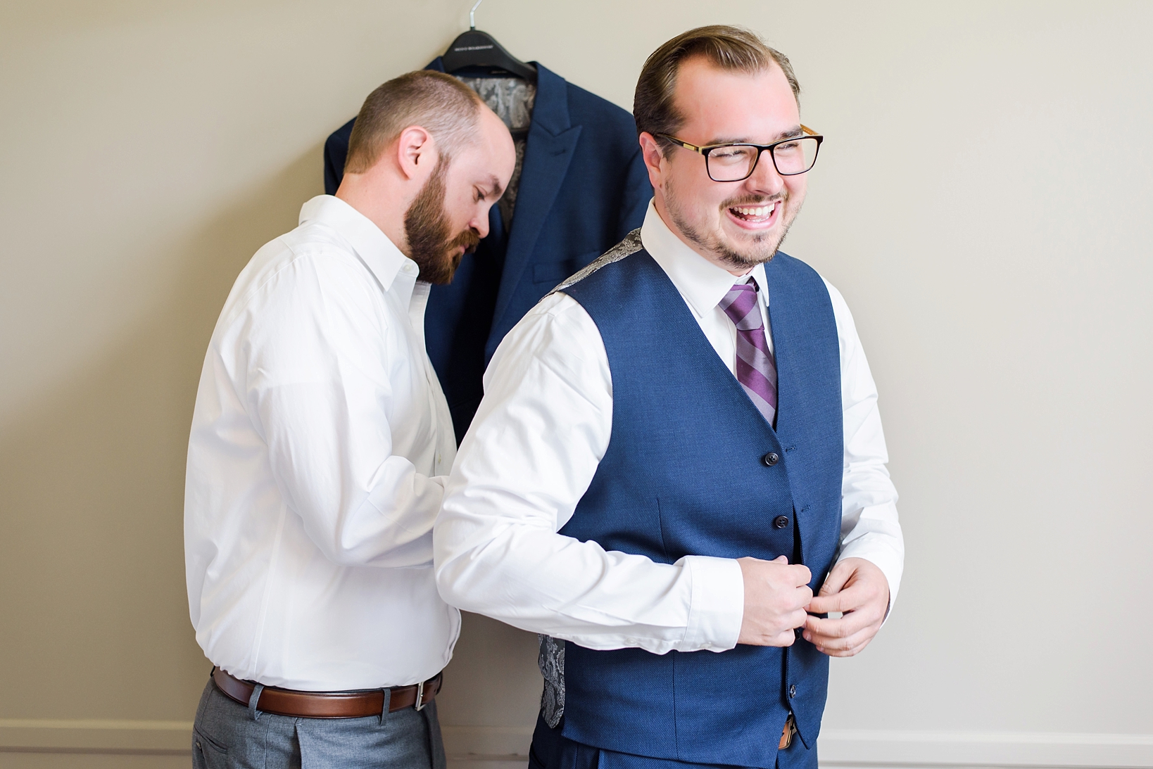 Groom laughs as he dresses for the ceremony by Sarah & Ben Photography