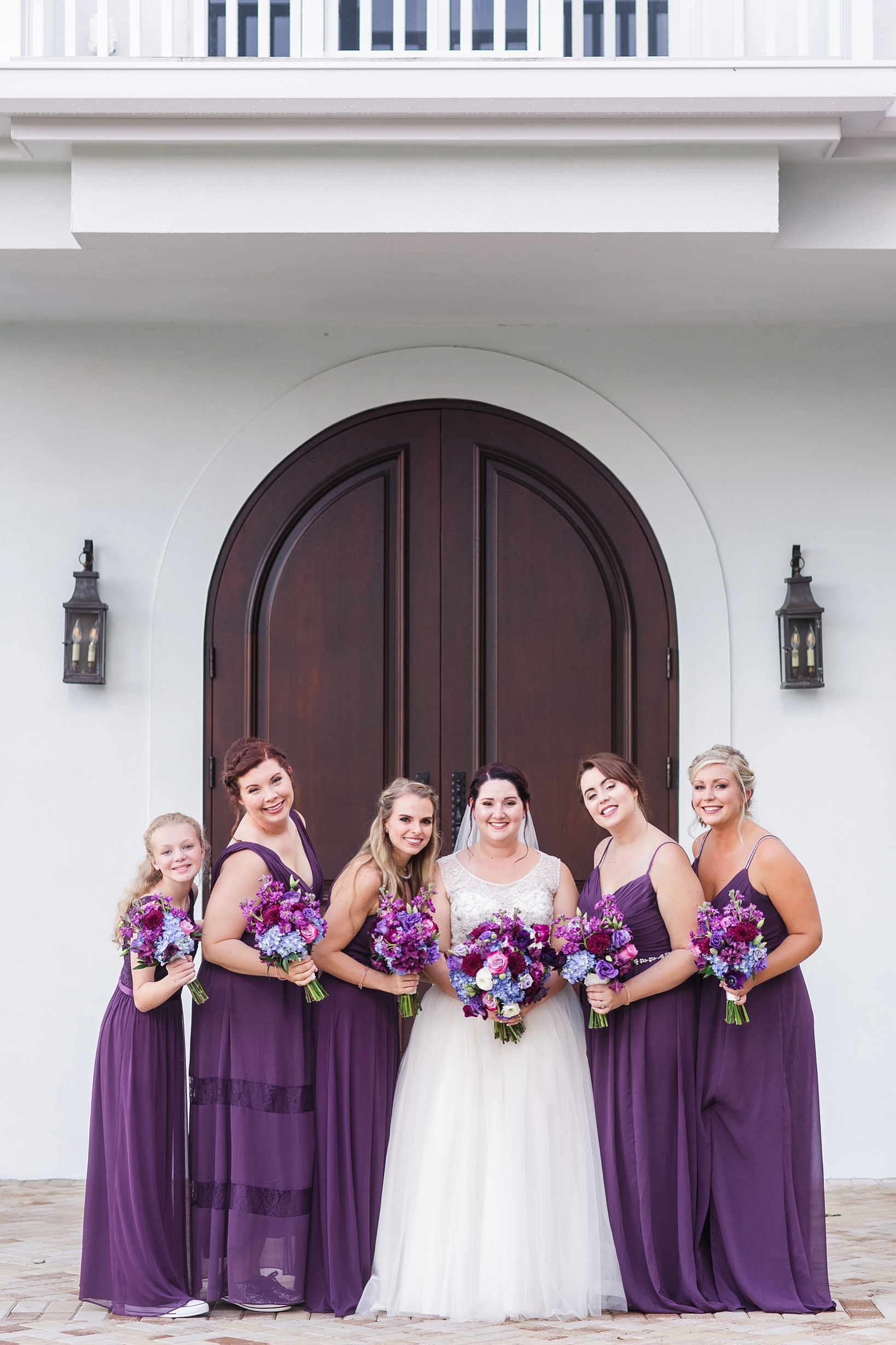 Bride and her bridesmaids pose in front of the chapel door by Sarah & Ben Photography