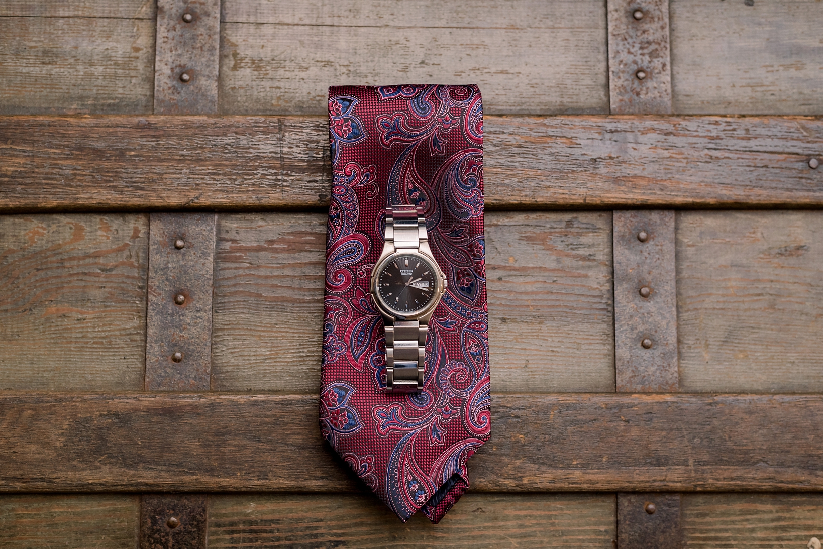 The groom's tie and watch on the wood top of a steamer trunk by Sarah & Ben Photography