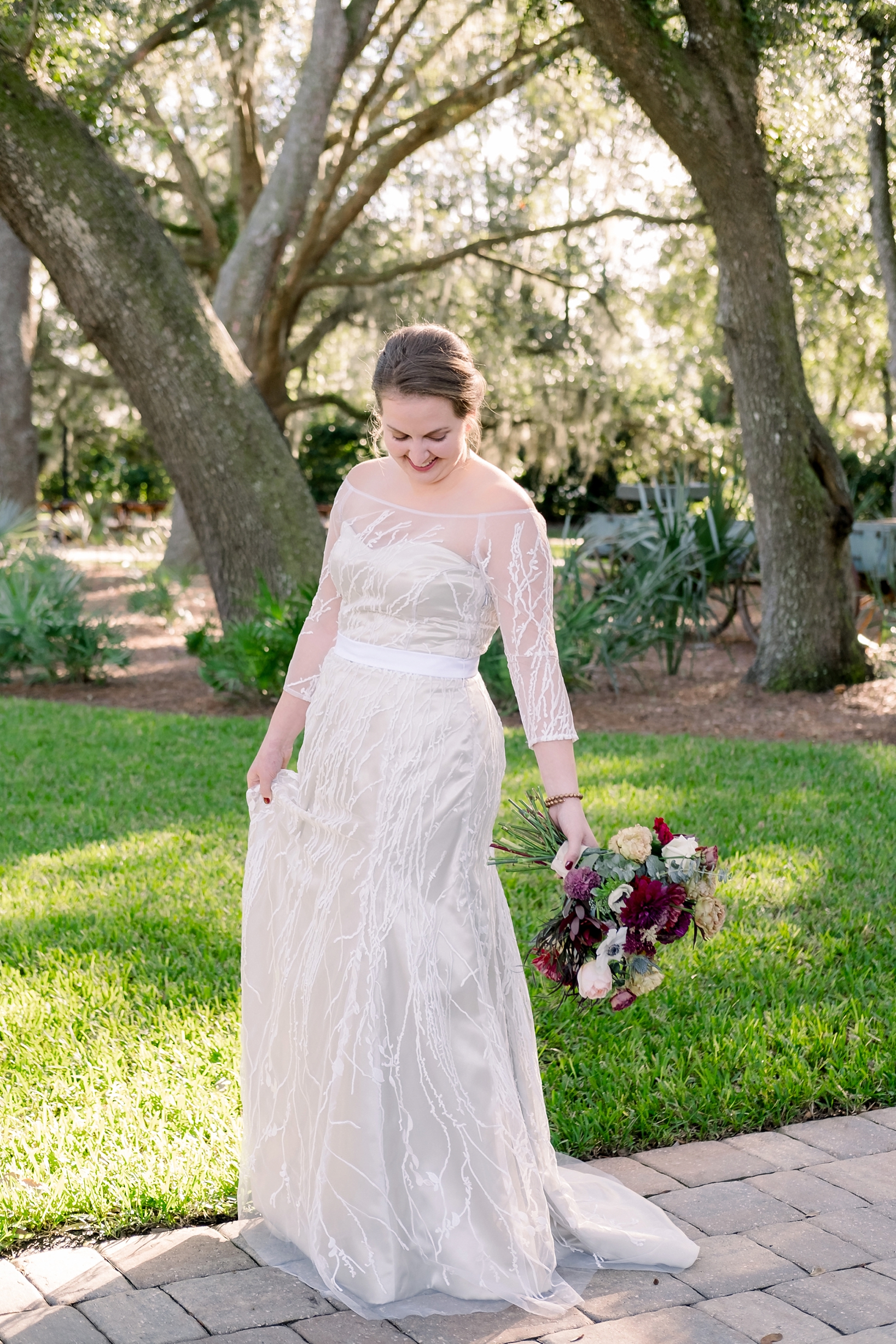 The Bride holding her dress and her bouquet as she walks a brick path by Sarah & Ben Photography