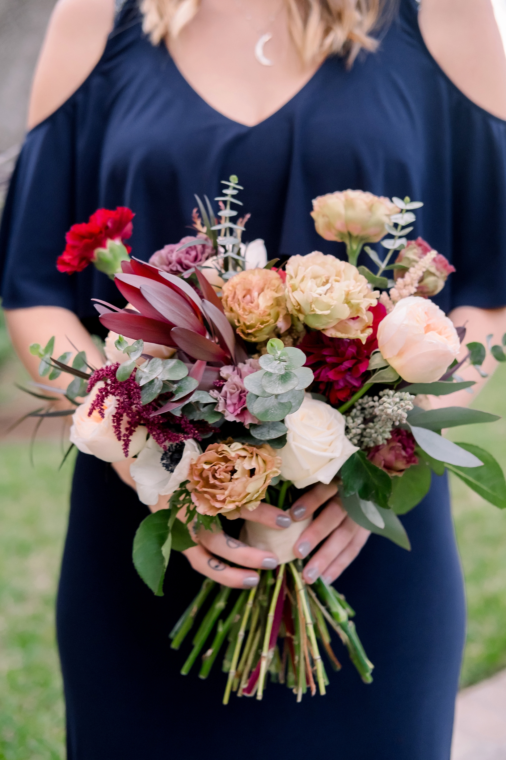 Maid of Honor holding her full bouquet of flowers against her Navy dress