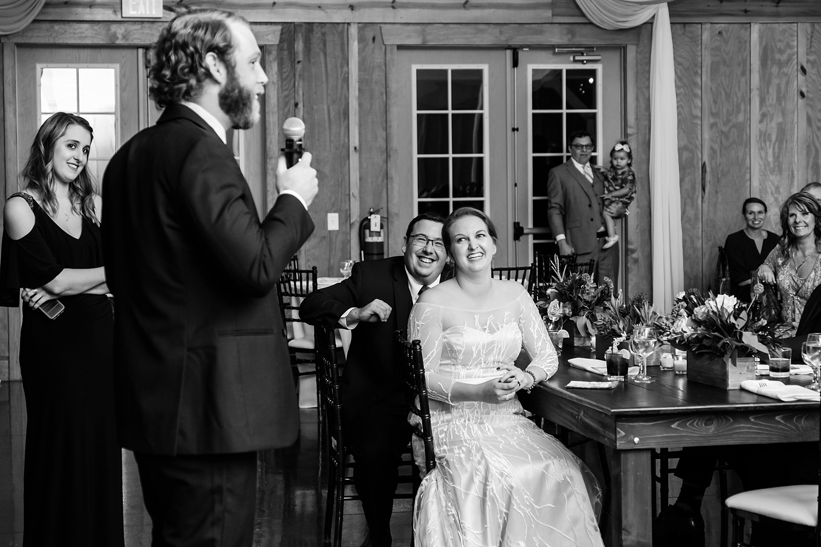 The wedding couple laugh as their friends give speeches to the reception hall