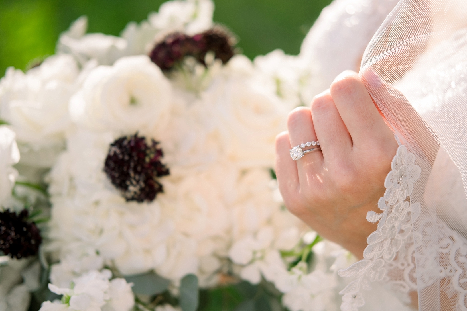 The bride's wedding ring glints in the sun surrounded by the lace of her sleeves by Sarah & Ben Photography