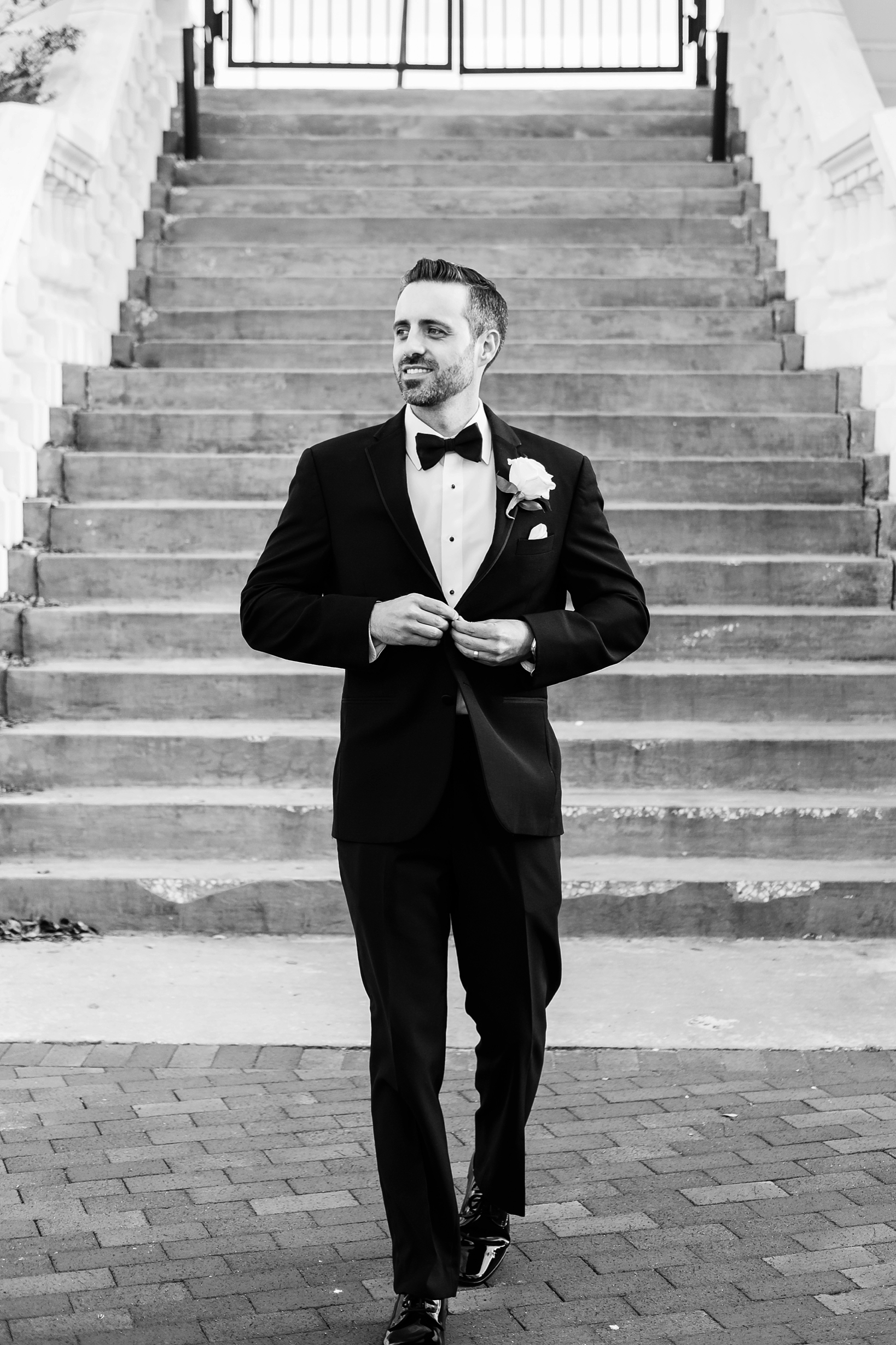 Portrait of the Groom buttoning his suit jacket in black and white by Sarah & Ben Photography