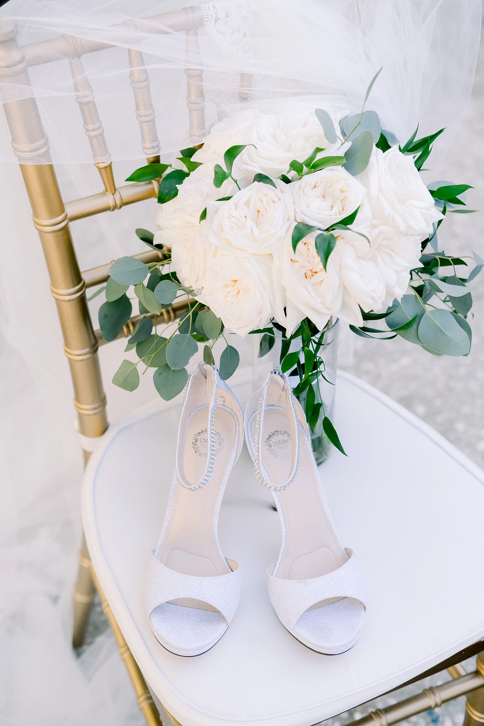 A bouquet of white roses and the bride's heels against a chiavari chair by sarahben.com