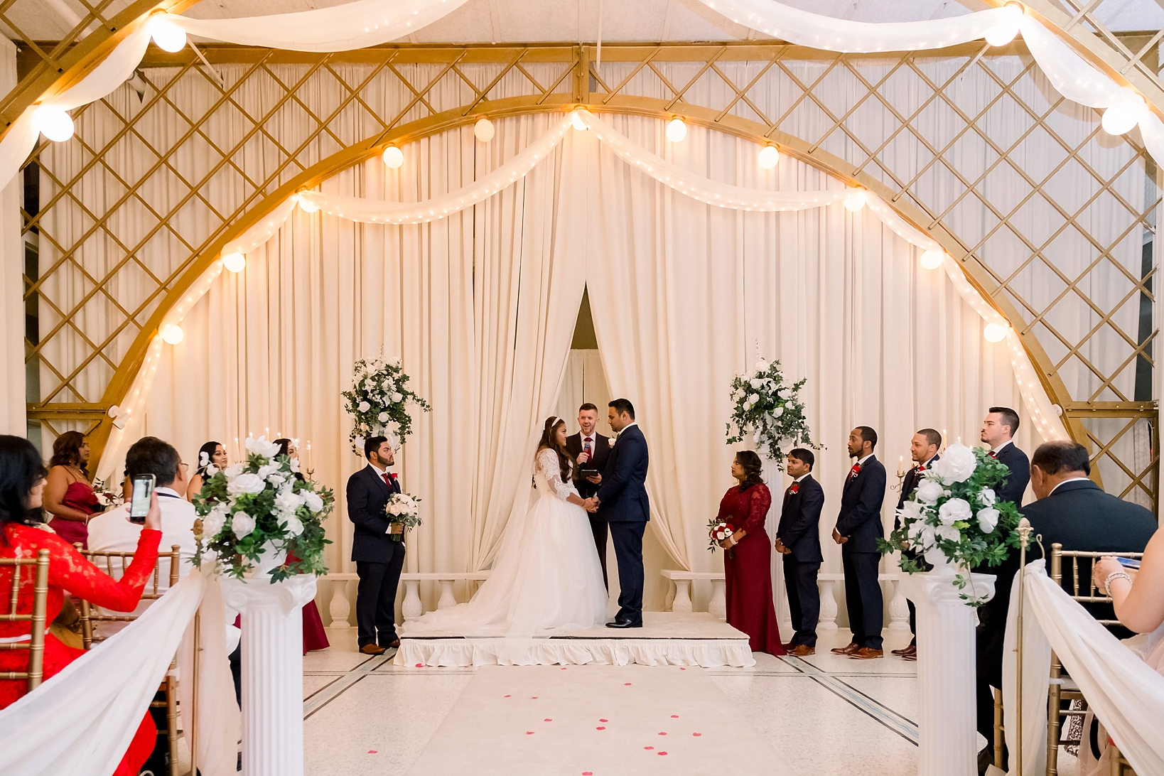 The bride and groom framed by the gold arches of the Kapok Tree's ceremony space by Sarah & Ben Photography