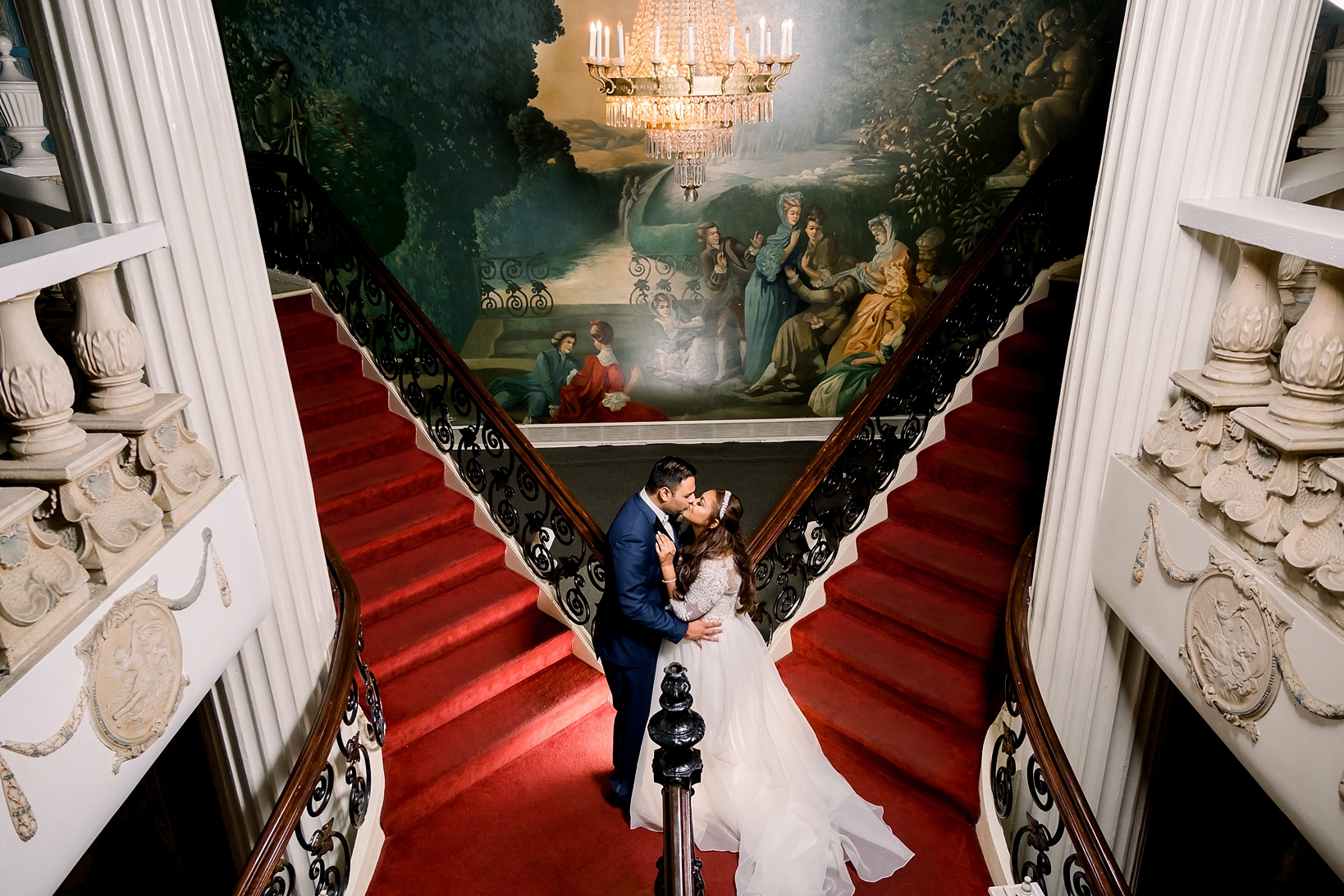 An epic staircase photograph of the bride and groom under a giant oil painting by Sarah & Ben Photography