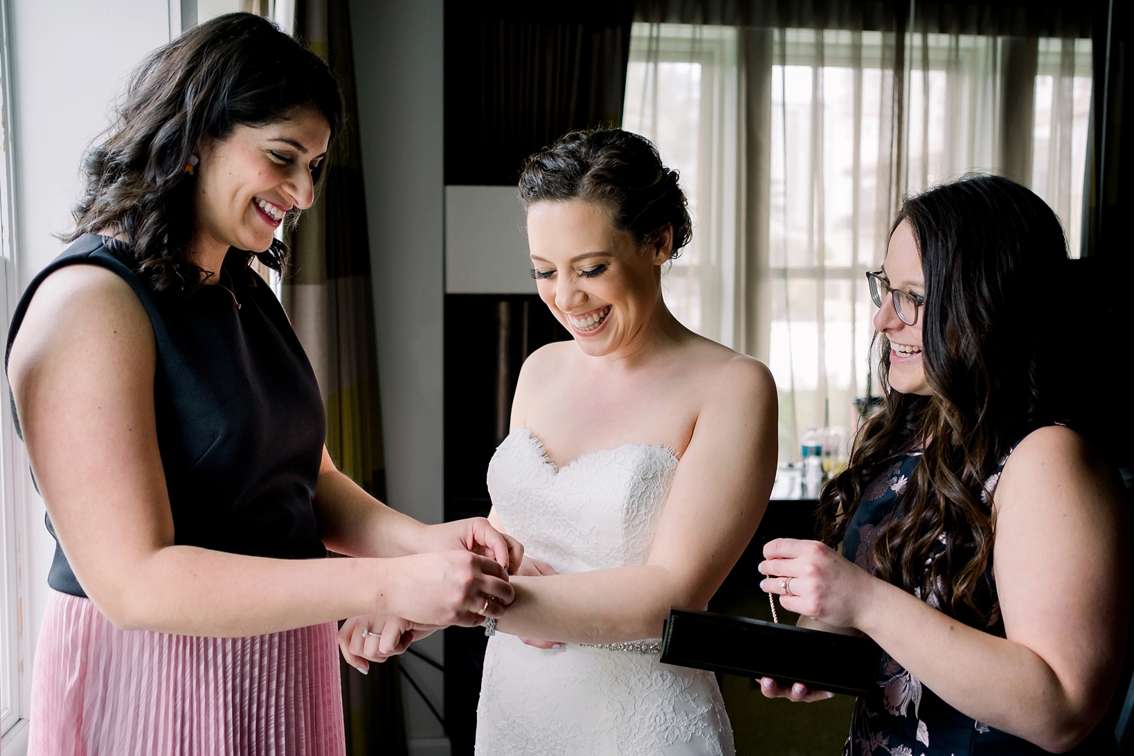 The Bride smiles as her friends help her with her wedding accessories by Sarah & Ben Photography