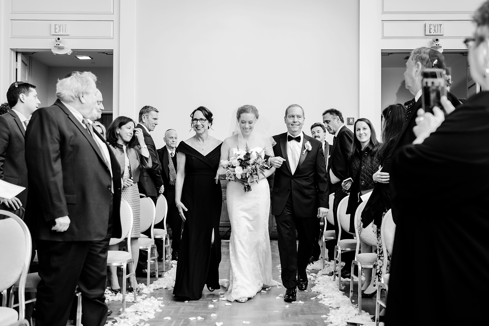 The Bride being escorted down the aisle by her parents in stunning black and white