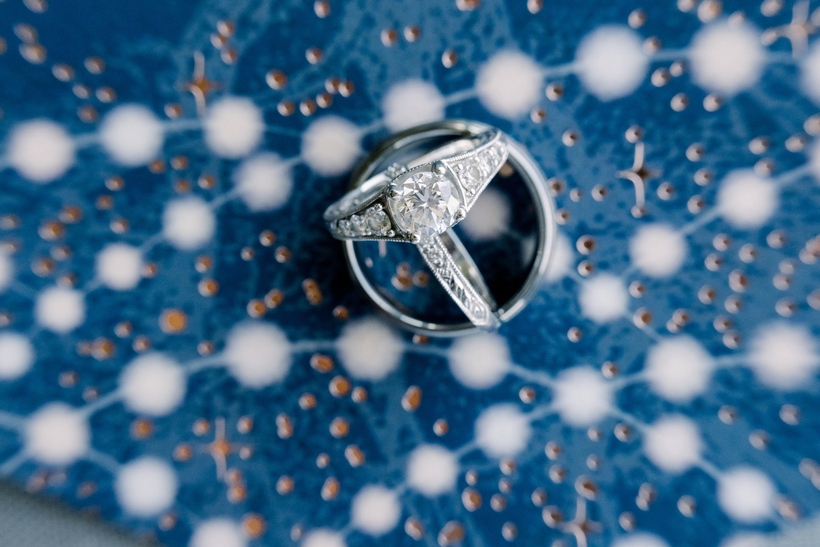 The wedding rings in front of a patterned background from the wedding invitation by Sarah and Ben Photography