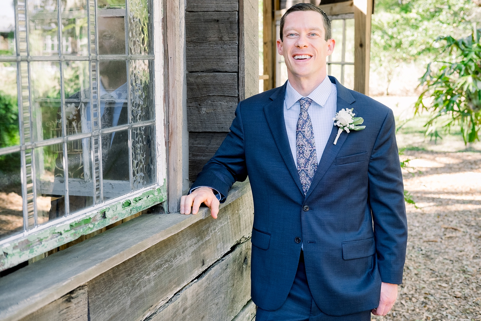 Groom leans against the barn on the Cross Creek Ranch property