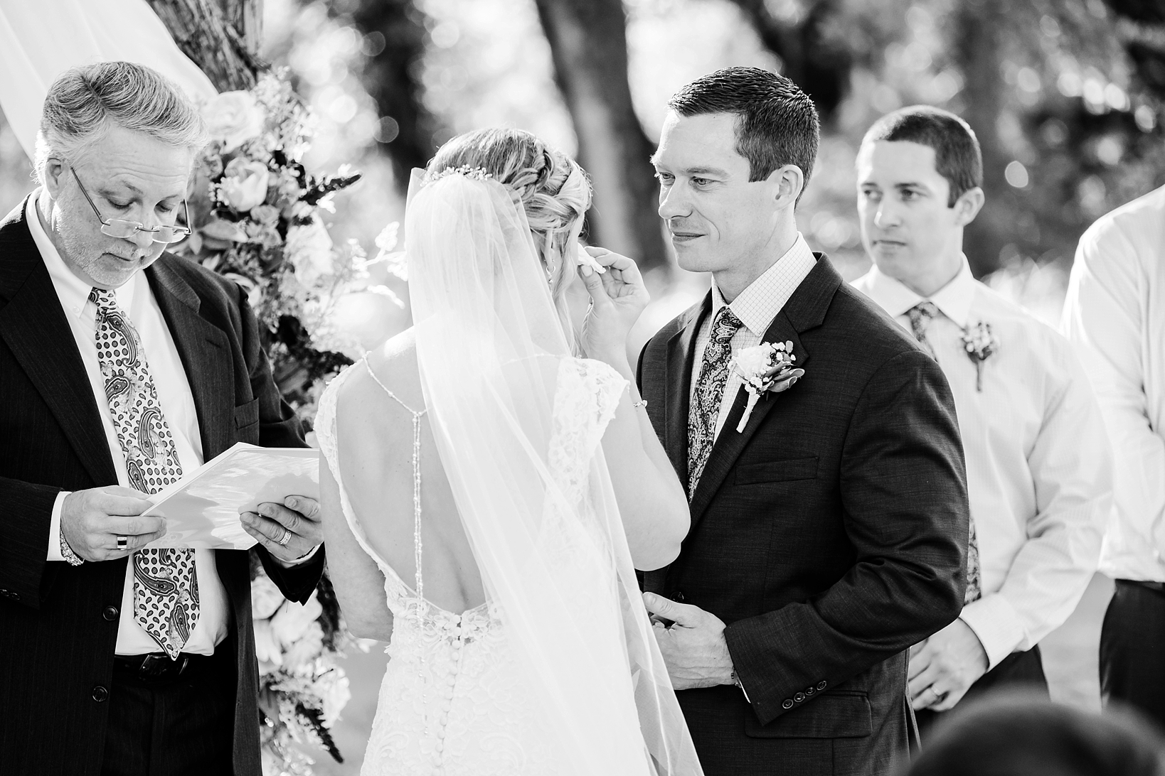 Black and white image of a Groom looking at his Bride during their wedding ceremony wipe away a tear