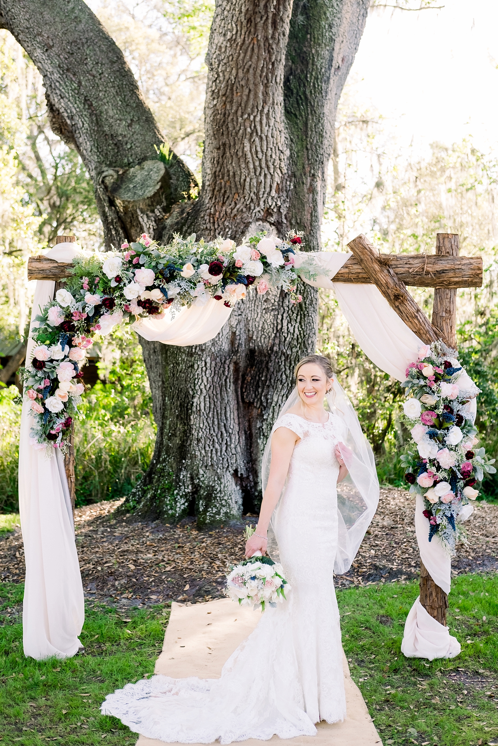 Solo portrait of the Bride holding her wedding bouquet under an oak tree and her wedding arch