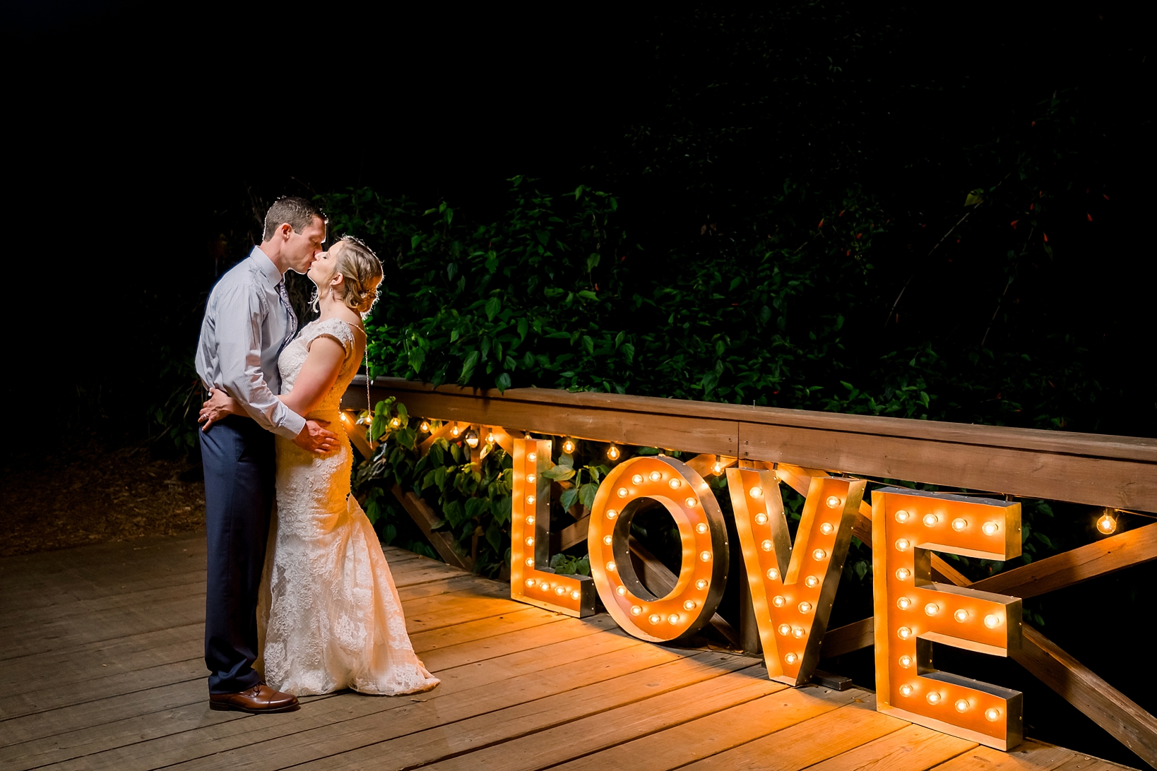 Groom and his Bride kiss next to the light up "Love" sign by Sarah and Ben Photography at Cross Creek Ranch