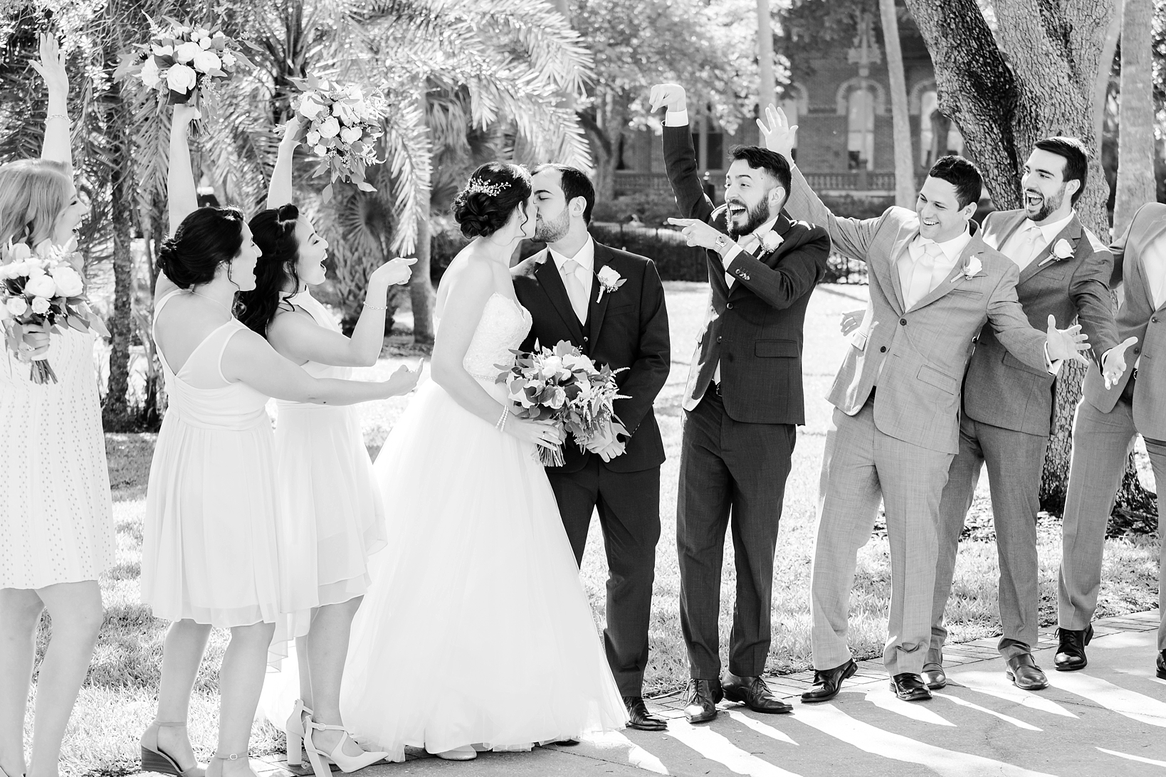 Black and white photo of the wedding party celebrating the newlyweds kissing