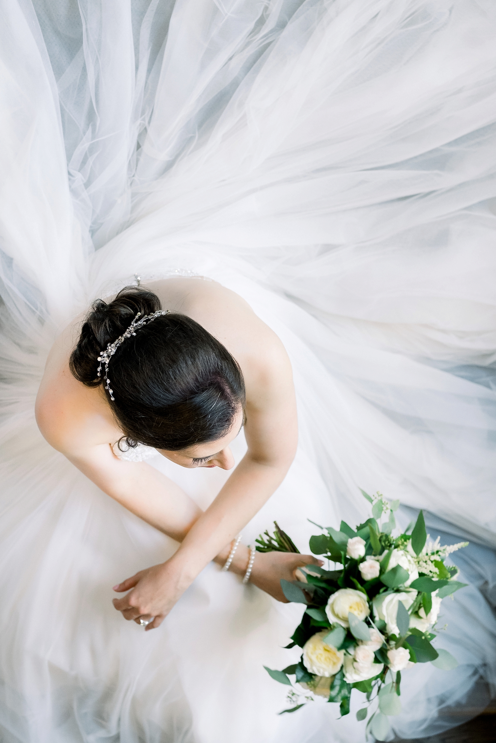 Bride from above with her wedding dress swirling around her as she sits holding her floral bouquet by Sarah & Ben Photography