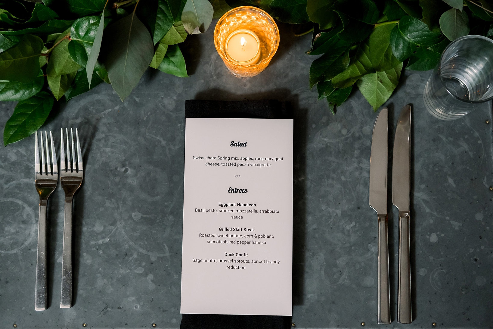 Reception menu and table settings surrounded by simple greeneries and tea lights