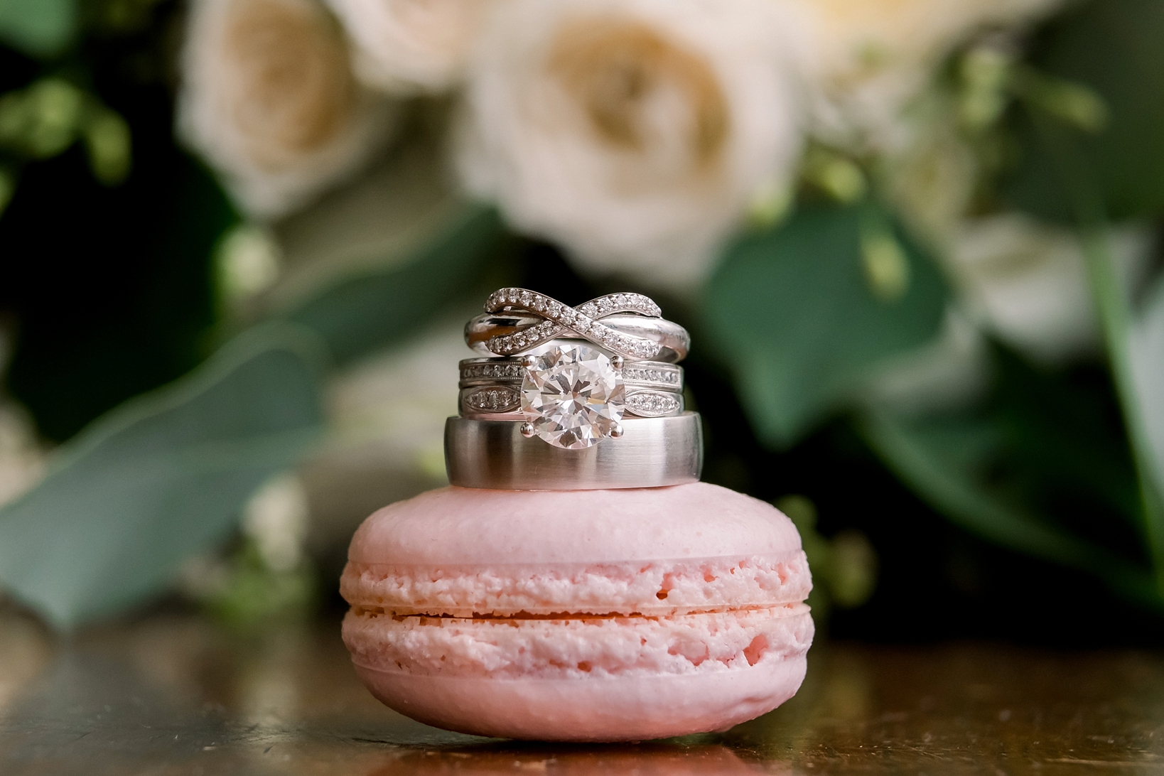 Close up photograph of the wedding bands on top of a macaron