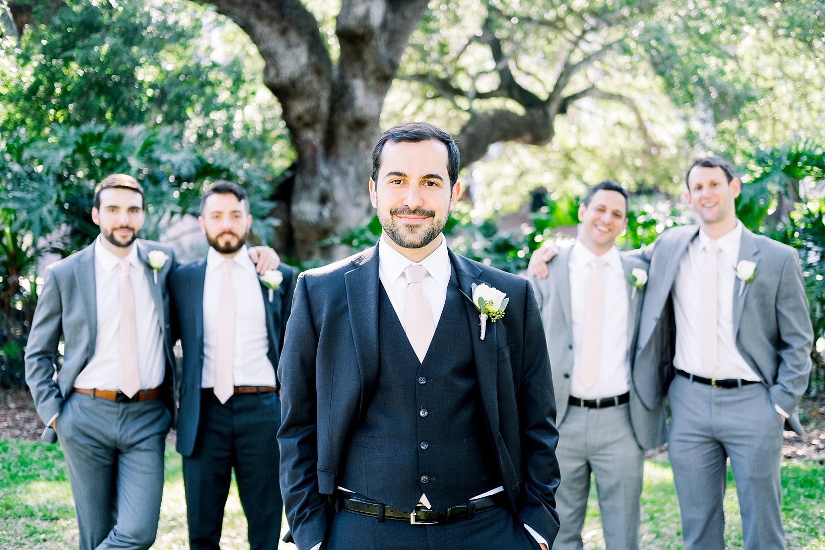Groom centered with his groomsmen on either side under the oak trees of the University of Tampa campus before his oxford exchange wedding day