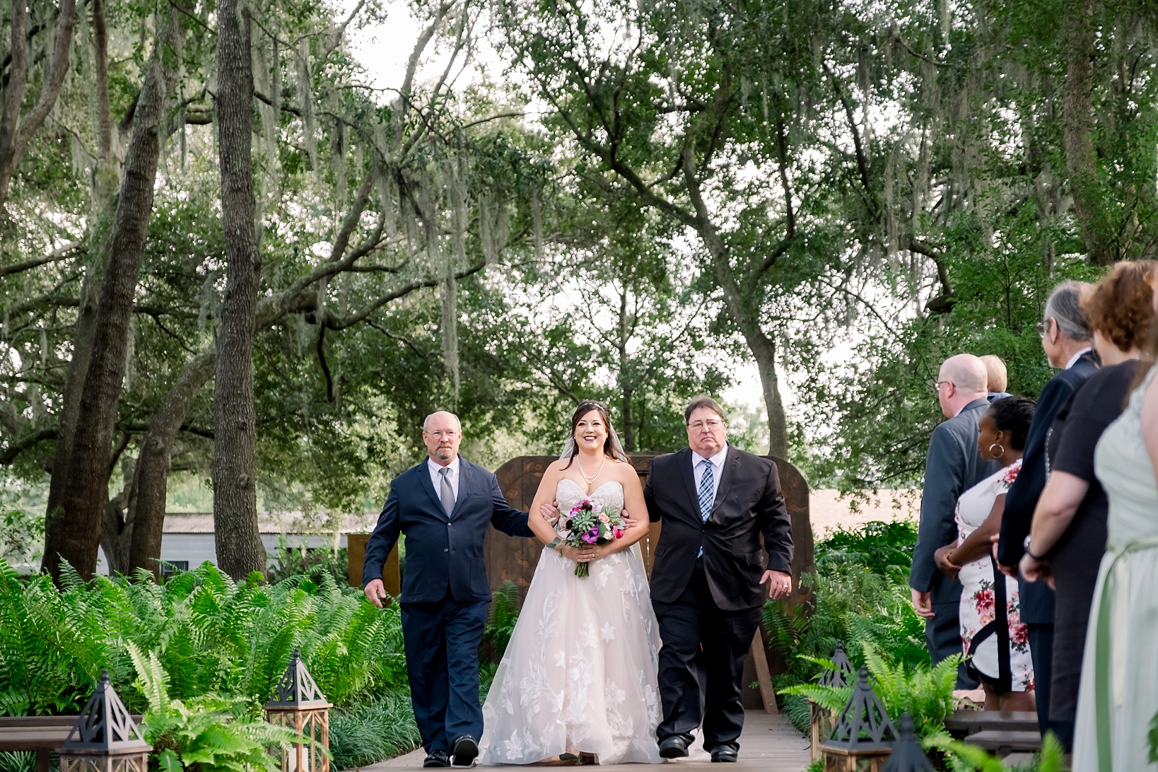 Bride walks down the aisle with her two dads on each arm during her cross creek wedding