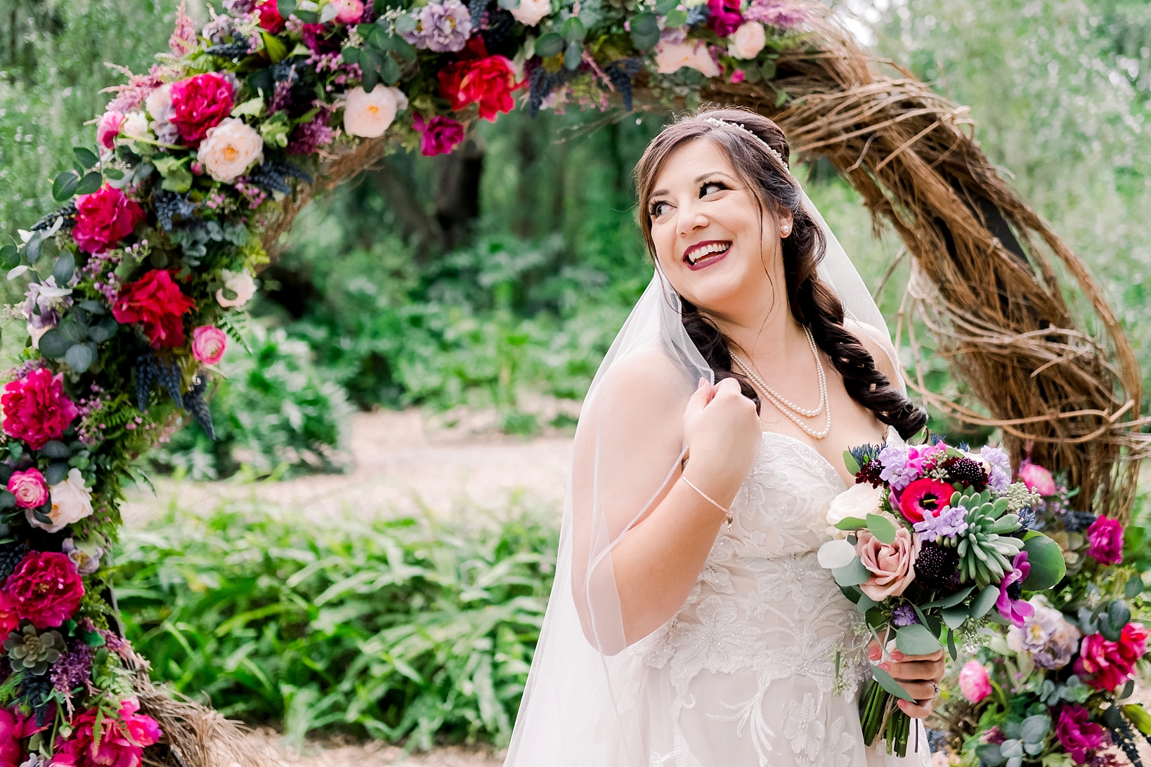 Bride poses for a formal portrait in front of her large floral altar while pinching her veil