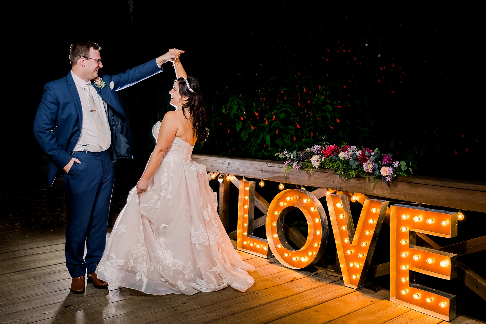 Bride and Groom dance on the bridge over Cross Creek next to a lit up sign that says "Love"